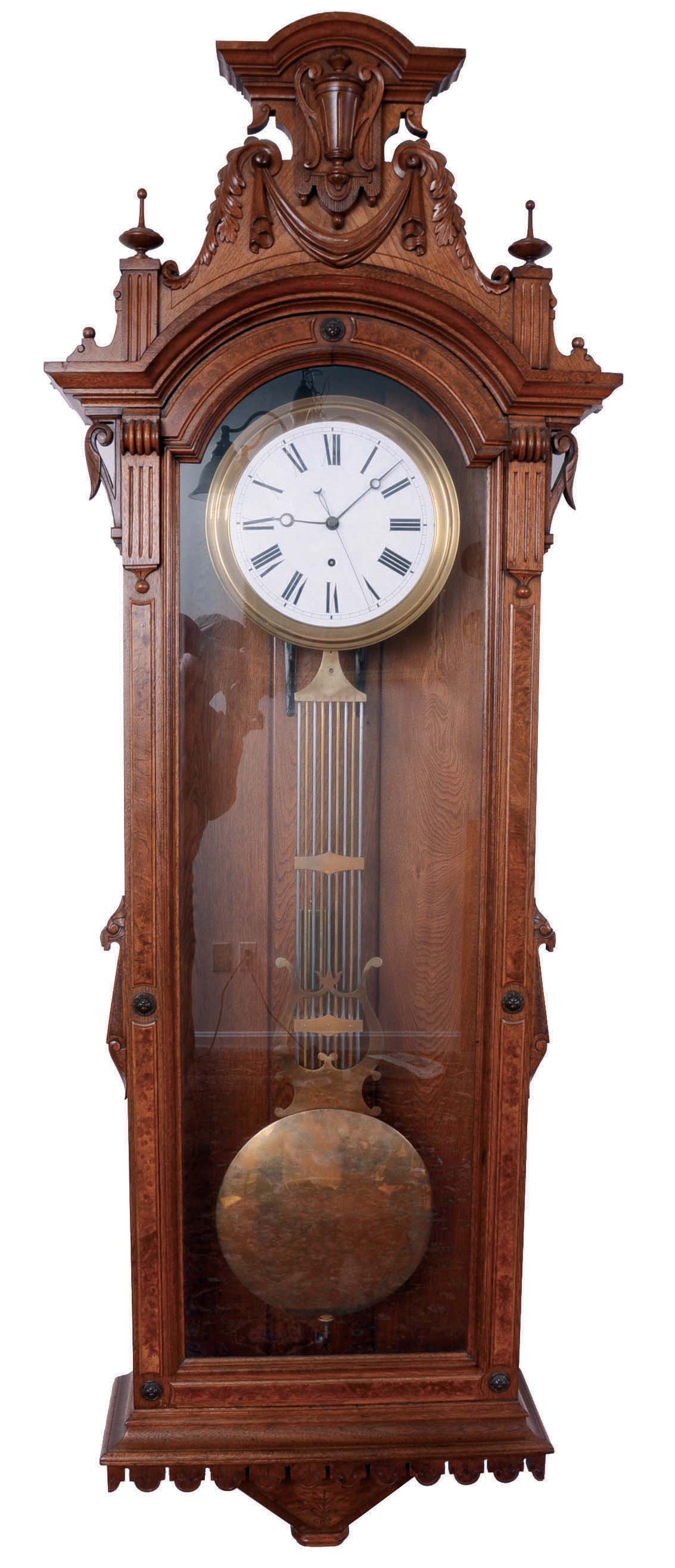 F. Kroeber & Co., New York, N.Y., "Regulator No. 27", jeweler's regulator wall clock, 8 day, time only, brass weight driven with Swiss pinwheel escapement timepiece movement, with a white enameled dial, a gridiron lyre pendulum and sweep seconds in a walnut case with burled accents and ornately carved top showcasing an urn in the center. — Antique Clocks Price Guide
