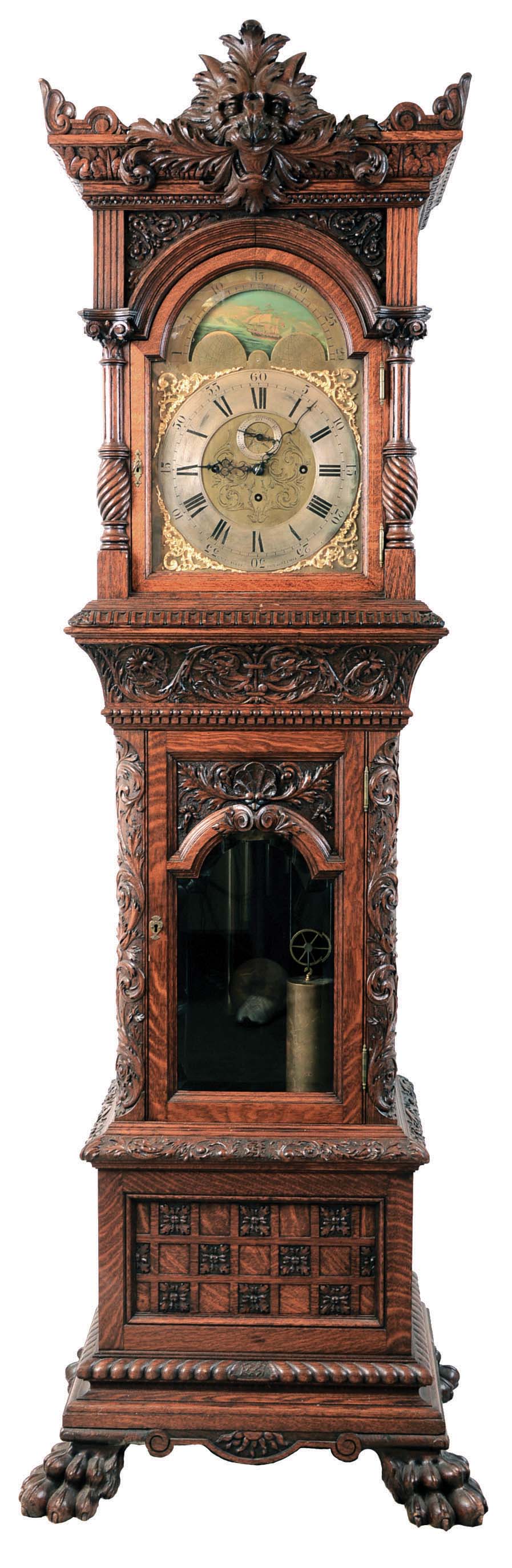Tall case clock retailed by G.W. Russell, Philadelphia, 8 days, time, strike and chime on 5 tubes, three brass weight driven movement in an ornately carved oak case attributed to R.J. Horner, New York with gargoyle top, fluted and turned corner columns topped by Corinthian capitals on hood, cut out frets, beveled glass doors, carved corner columns, two raised panels on each side, resting on a base with checkerboard panels on sides and front on huge furry paw feet. The engraved brass dial has applied corner spandrels, silvered chapter and second's rings and moon phase. — Antique Clocks Price Guide
