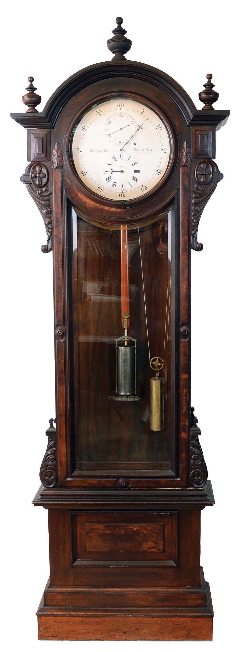 George Fitts, Bangor, Maine, standing astronomical jeweler's regulator, 8 day, time only, weight driven movement with sapphire pallets, Graham deadbeat escapement, maintaining power, counter weighted crutch pin fitted closely to a bushing in pendulum rod, German silver bushings with closed ends with integral end pieces and eccentric bushings for the pallet arbor in a walnut and burled walnut carved case with domed top and three finials, beveled glass trunk door and raised burl panel on base. The silvered astronomical dial is signed and dated 1847 by maker. — Antique Clocks Price Guide