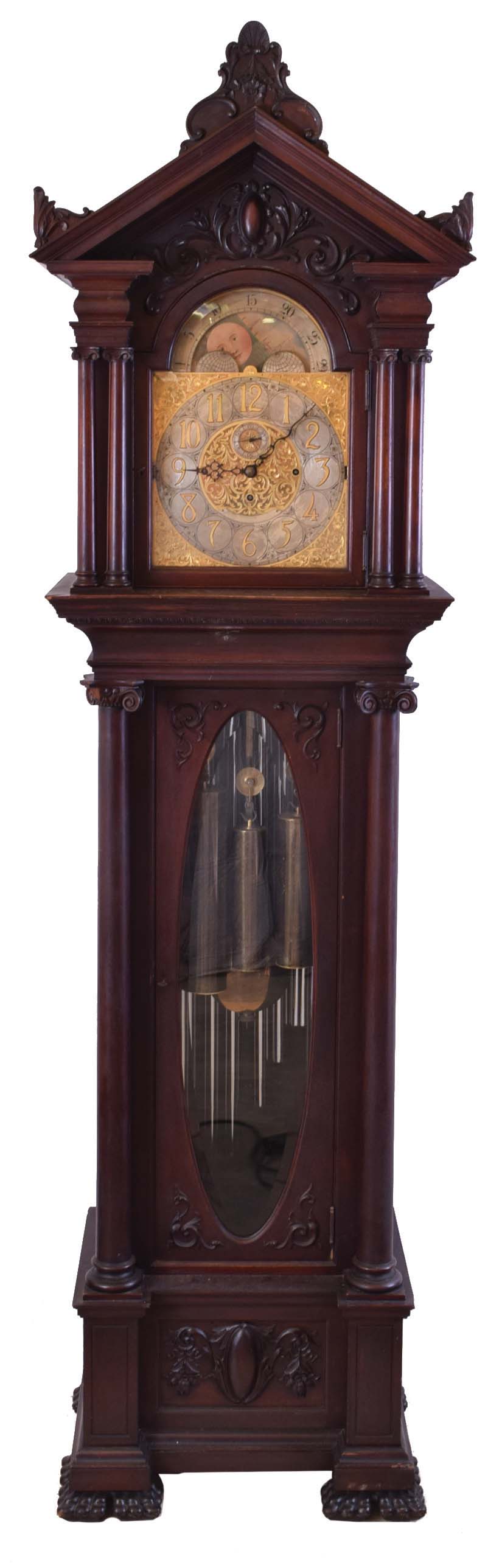 England tall clock with tubular bells retailed by Bigelow, Kennard & Co., 8 day, time, strike and chime on 9 tubular bells playing Westminster and one other tune, three brass weight driven movement in a mahogany case with pediment top and side and center carvings. The tympanum above the dial has applied carved moldings, the hood door has double columns on each side with carved volute capitals over the trunk with full columns flanking beveled glass door with carved volute capitals resting on a base with applied carved moldings and paw feet. The brass dial has applied brass numerals over a silvered chapter ring and silvered second's bit, ornately engraved spandrels and dial center, moon phase, strike / silent and tune selectors. — Antique Clocks Price Guide