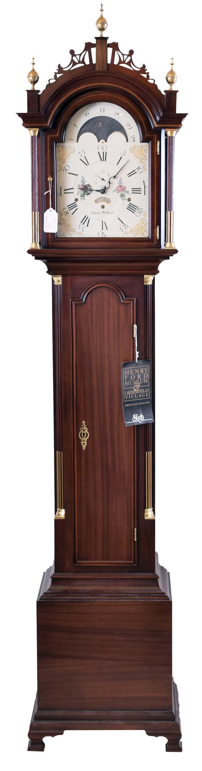 The Henry Ford Museum, Dearborn, Michigan reproduction Simon Willard, Boston, Mass., tall case clock, 8 day, time, strike and triple chime, weight driven movement in a mahogany Roxbury style case with three brass finials, fretwork top, fluted full columns on hood with brass terminals, string inlay, fluted corner columns on trunk with brass terminals, ogee feet and moon phase dial — Antique Clocks Price Guide