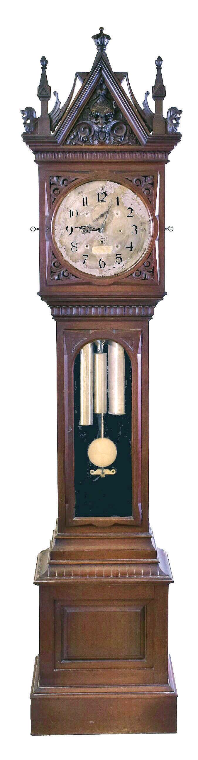 E. Howard & Co., Boston, No. 77 hall clock with Westminster chimes, mahogany case, the molded base with inset panel, trunk door with fan carved corners and beveled glass, the interior lined with black flocked paper, and bonnet with carved grotesque mask, gryphons, and gothic style pinnacles, 14 inch, Arabic numeral silvered dial, blued steel English pattern hands, 8 day, three train movement with Graham deadbeat escapement, full Westminster chiming, stopwork on all trains, and counting the hours on a gong, brass weights, heavy brass pendulum with gilt cherry rod — Antique Clocks Price Guide