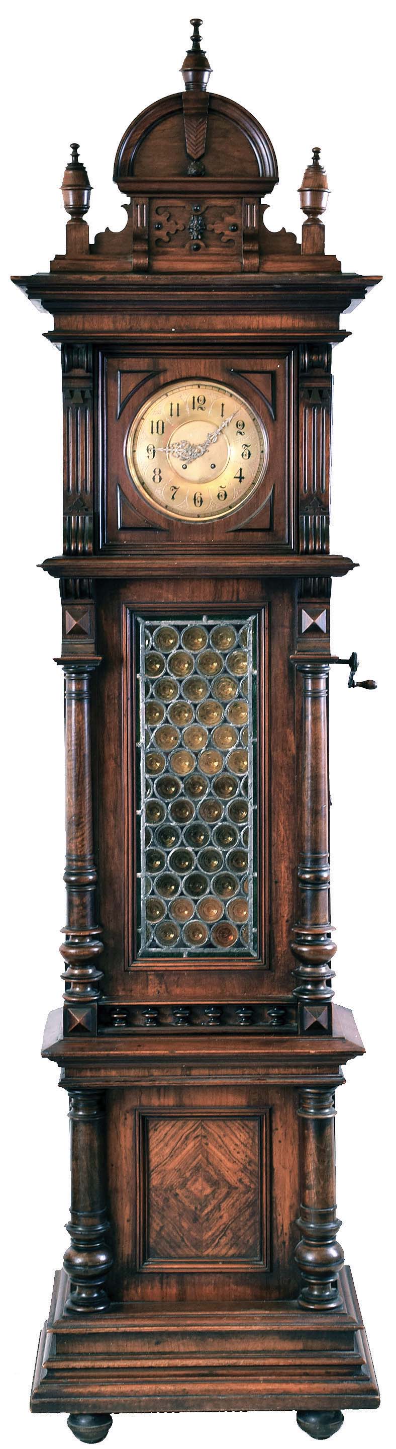 Polyphon Musicwerke, Leipzig, Germany, "Style No. 61" tall clock with music box, 14 day, time and strike, spring driven Lenzkirch movement with Polyphon single comb music box playing 15 3/4" discs hourly. The music can also be started at will by coin operation or silenced. The case of walnut is Grunderzeit styled and highly carved with antique leaded blown glass trunk door. The dial is brass with pierced steel hands. Includes seven Polyphon discs. — Antique Clocks Price Guide