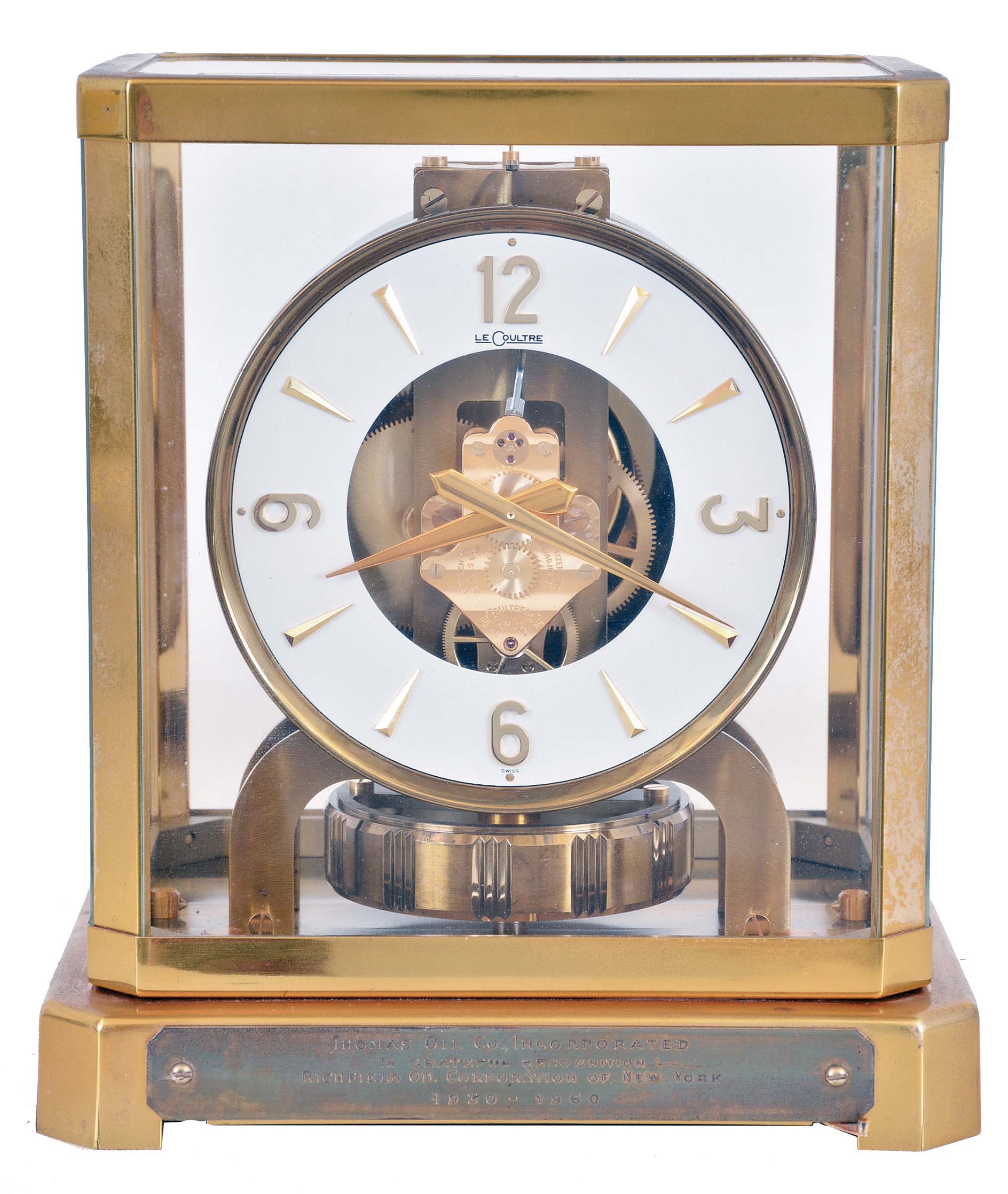 LeCoultre & Cie, Switzerland, "Atmos" clock, 15 jewel gilt caliber 528 movement, gilt torsion pendulum, round white painted dial with applied gilt Arabic numerals and arrow markers, gilt hands, all contained in a glazed rectangular case with removable top, presentation plaque mounted to front of base, with Atmos pamphlet, serial #123665 — Antique Clocks Price Guide