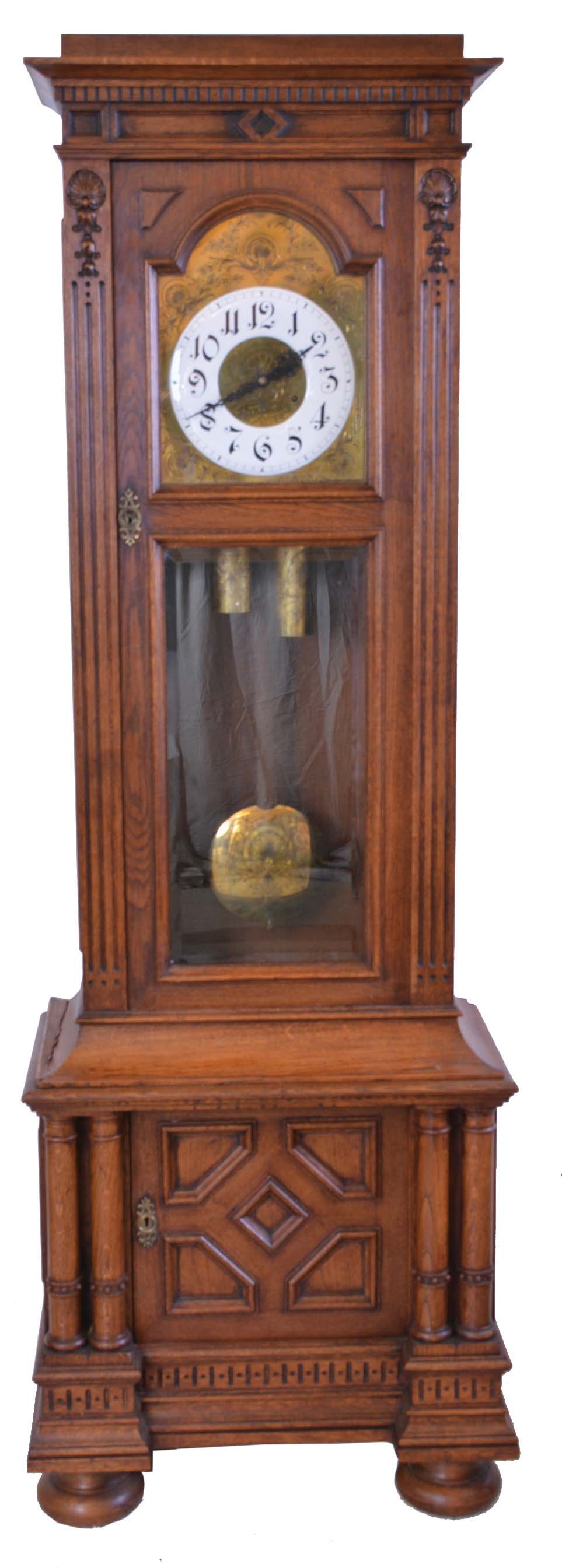 Germany, tall clock, 8 day, time and strike, two brass weight driven movement in a carved oak case, beveled glass door, cabinet in base on bun feet with engraved brass dial with white enamel chapter ring and matching engraved weights, pendulum and dial center — Antique Clocks Price Guide