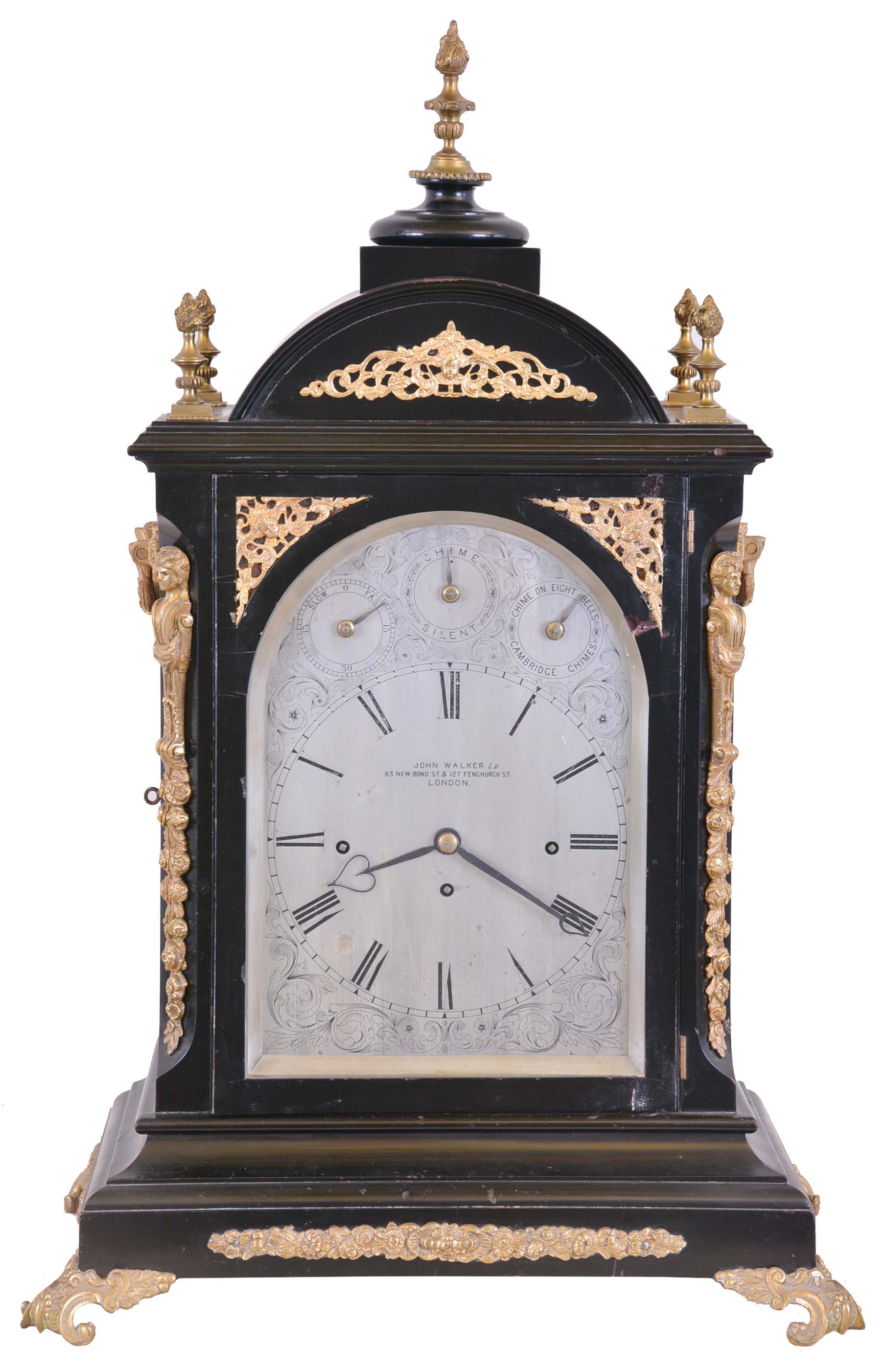 John Walker Ltd., London, large bracket clock, ebonized case with caryatid corners, and set with cast, gilt mounts and ornamental scroll feet, the sides with cast, pierced frets with Helios mask, and foliate ornamented carrying handles, case top with five finials; engraved, silvered sheet brass Roman numeral dial, the arch with controls for regulation and chiming, blued steel hands, large three train fusee movement, with Cambridge Chime or Chime on Eight Bells at the quarters, and counting the hours on a large gong, dial and movement signed — Antique Clocks Price Guide