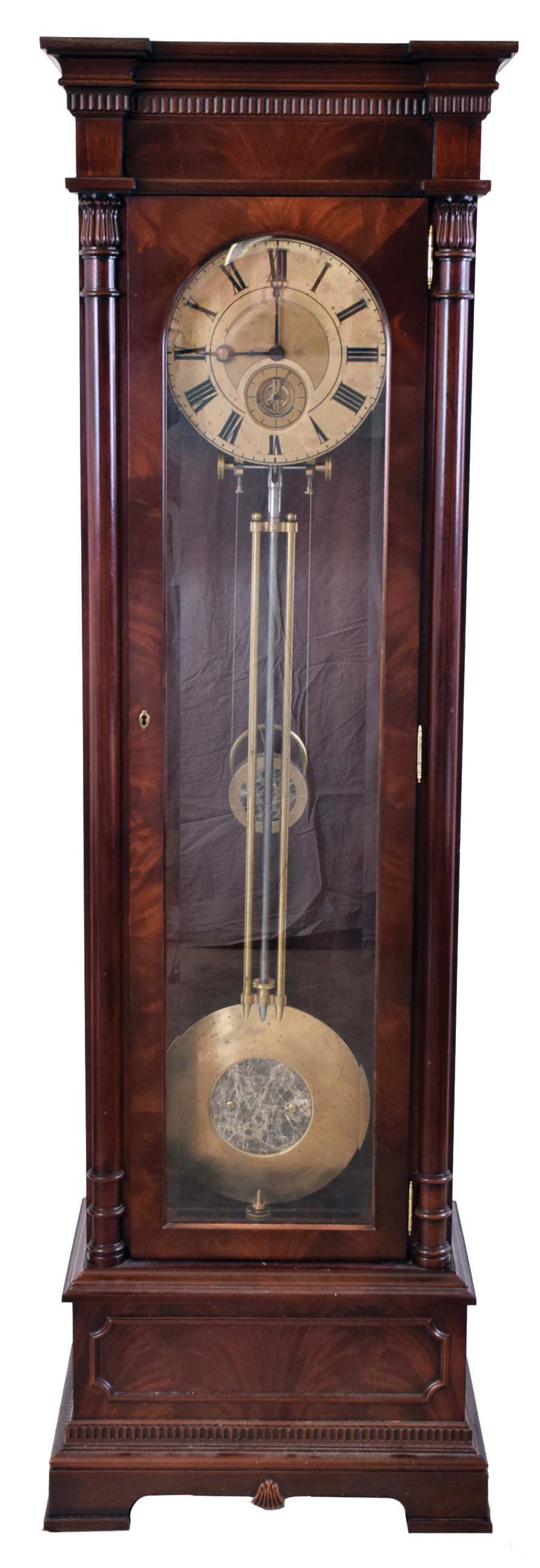 Standing regulator, polished mahogany and mahogany veneer case, Roman numeral brass dial with aperture below the center arbor for viewing the escapement eight day weight driven movement with high count, five wheel train, crutchless Graham deadbeat escapement, and beveled glass dust shields, heavy, bi metallic pendulum with 12", stone inlaid lenticular ball and the pallets rigidly attached at top of rod, integral suspension with beat adjustment, disc shaped weight also with stone inlay — Antique Clocks Price Guide