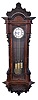 Vienna regulator, large, angular case with wanut veneers and framed burl walnut veneer panels, carved crest and base, cast bezel with two piece Roman numeral white enamel dial, blued steel hands, three train, quarter striking movement, with brass and steel gridiron pendulum and brass weights