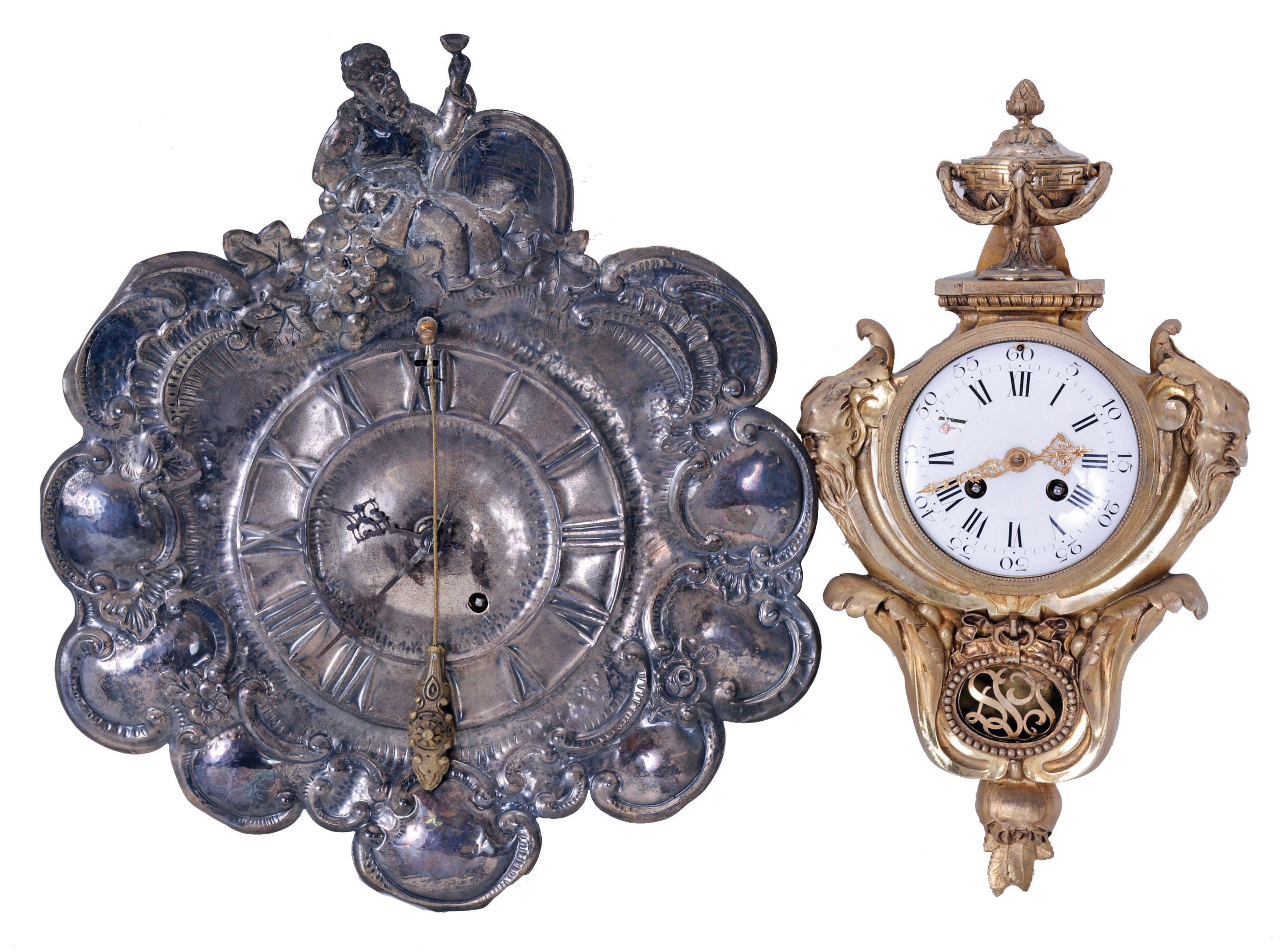 Clocks- 2 (Two): (1) a French cartel clock, ornate gilt case with foliate ornament, urn finial, and Green Man masks flanking the Roman numeral, white enamel dial, 8 day, time and strike, pendule de Paris movement; (2) Silvered, repousse "shield" front wall timepiece, decorated with c scrolls, and tippling vintner at top, Roman numeral dial, and cow tail pendulum, 8 day Japy Freres movement, dimensions of cartel listed — Antique Clocks Price Guide