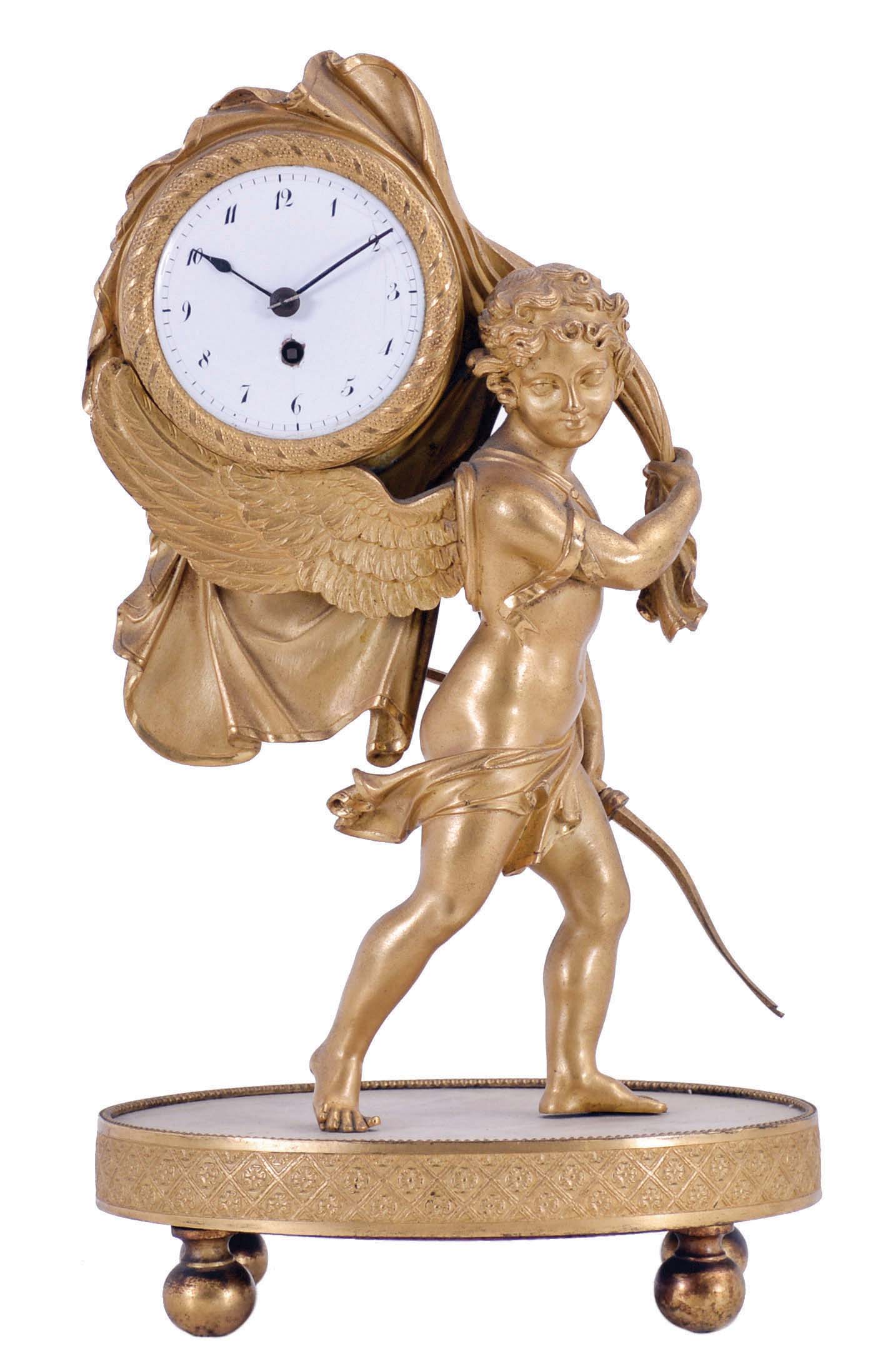 France, a small, gilt bronze desk or table clock, the figure of Cupid carrying a bow in his left hand, while his right hand draws back a sheet revealing the clock atop his wings, all on a dore bronze trimmed marble base with gilt feet, Arabic numeral white enamel dial, now with later, 8 day timepiece movement with cylinder escapement — Antique Clocks Price Guide