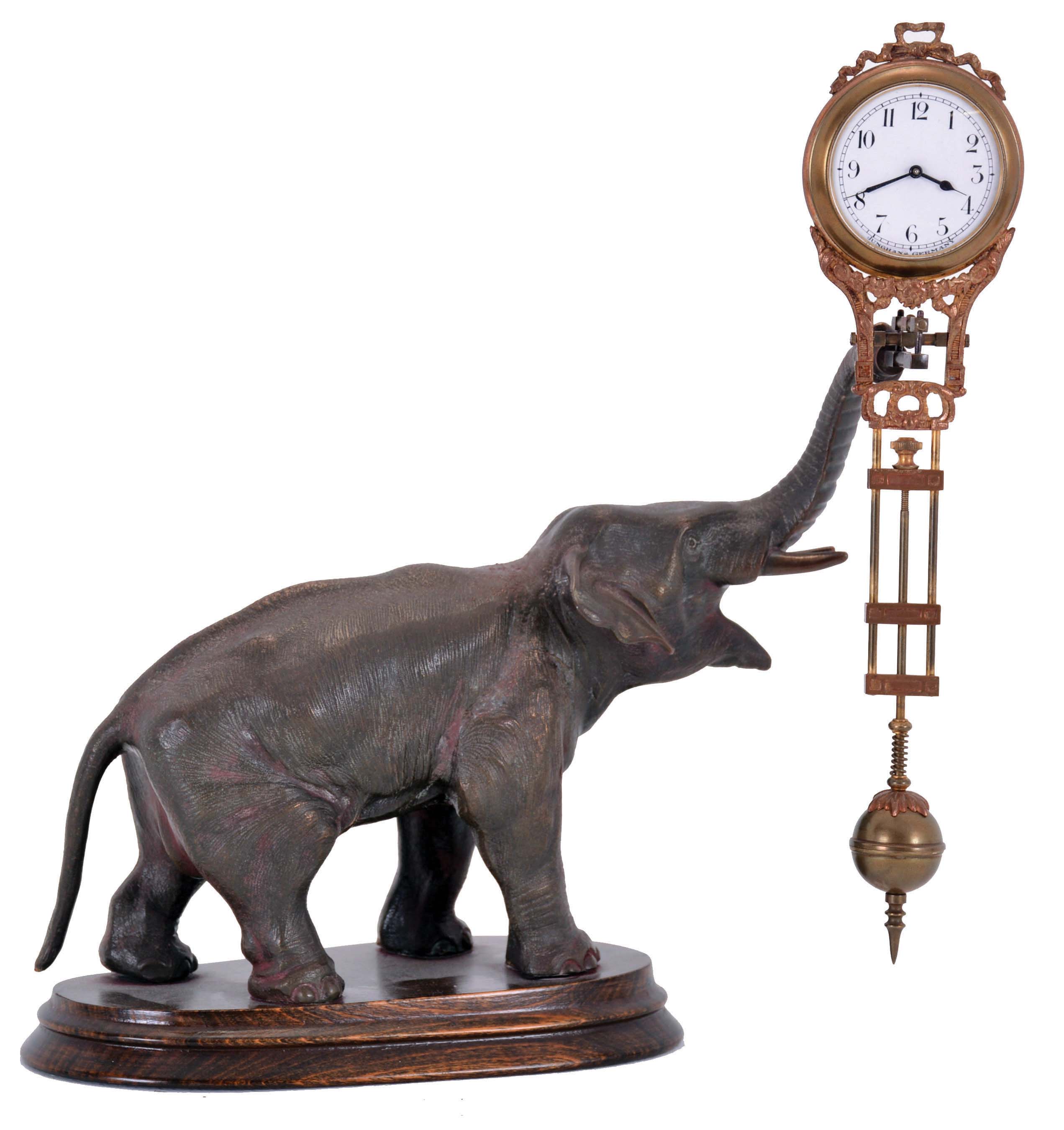 Junghans, Germany, elephant model swinging clock, patinated figure of an elephant mounted to a molded beechwood base, the 8 day swinging timepiece held aloft at the end of his trunk, clock case with gilt and patinated surfaces, Arabic numeral white enamel dial signed "Junghans Germany" below 6:00, blued steel hands, 8 day time only movement — Antique Clocks Price Guide