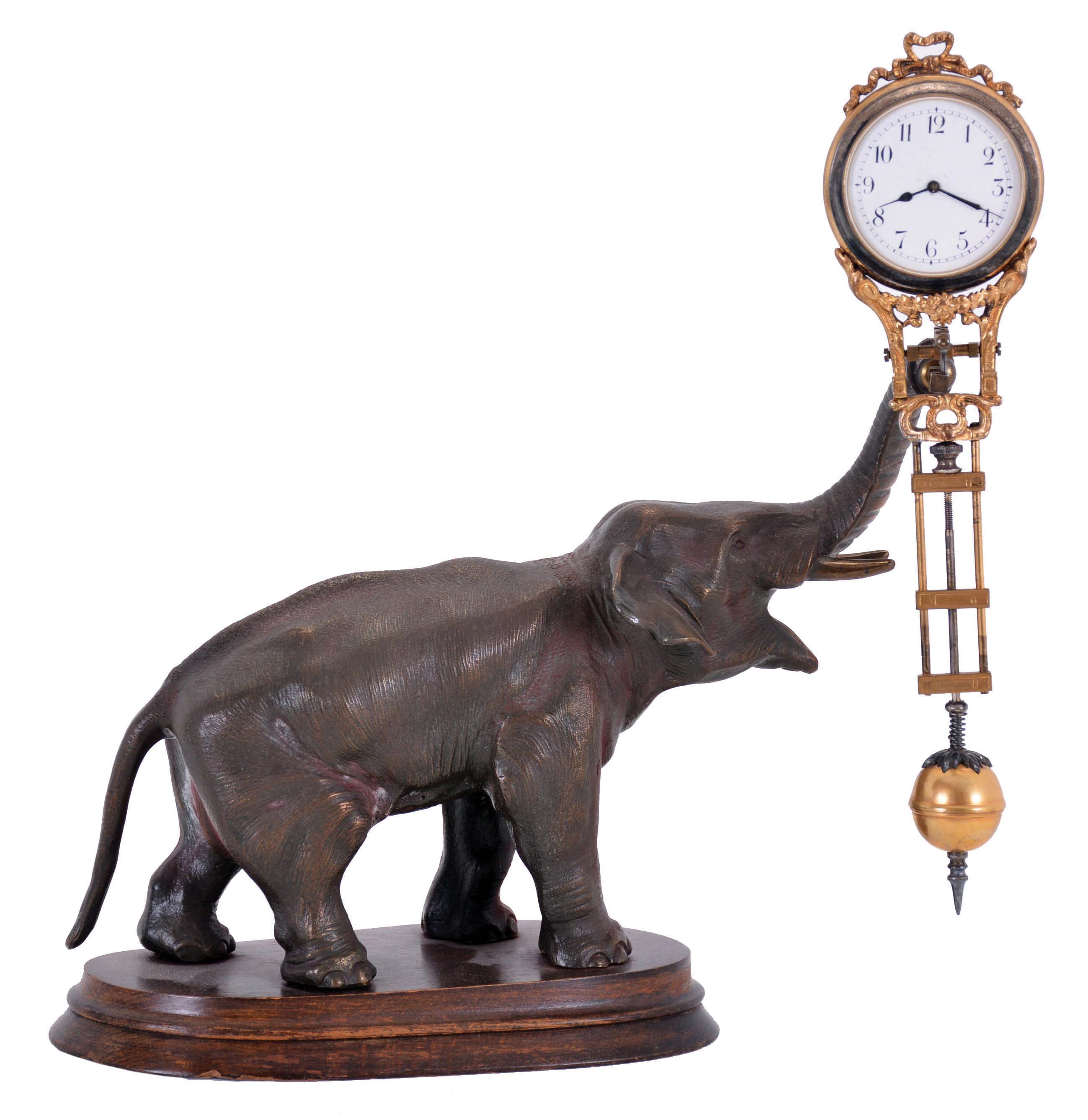 Junghans, Germany, elephant model swinging clock, patinated figure of an elephant mounted to a molded beechwood base, the 8 day swinging timepiece held aloft at the end of his trunk, clock case with gilt and silvered surfaces, Arabic numeral white enamel dial, blued steel hands, 8 day time only movement — Antique Clocks Price Guide