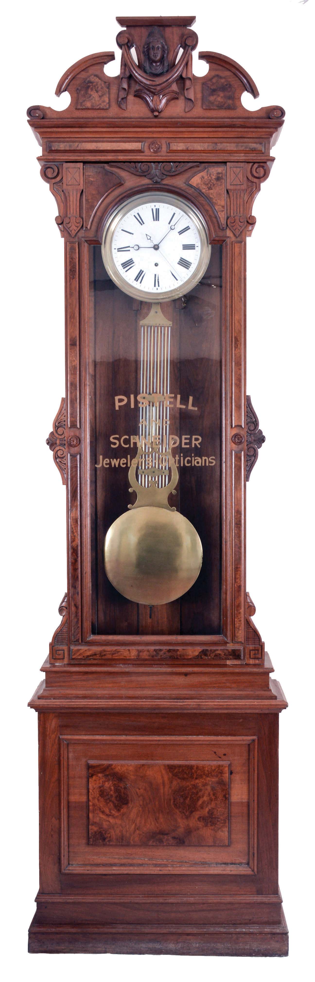 New Haven Clock Co., New Haven, Conn., "Regulator No. 4", jeweler's regulator floor standing clock, 8 day, time only, weight driven movement with Swiss pinwheel escapement and gridiron lyre pendulum in a walnut case with burled walnut highlights with jeweler's private label "PISTELL AND SCHNEIDER JEWELERS-OPTICIANS" stenciled on front of trunk door and Jenny Lind crest with a white enamel dial and center sweep seconds — Antique Clocks Price Guide