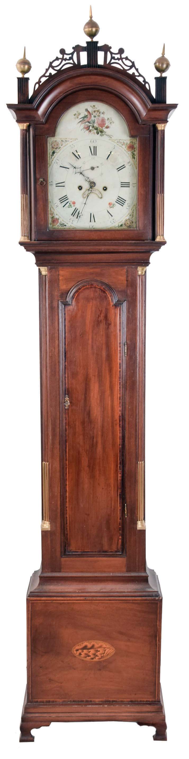 Unsigned Roxbury style tall clock, mahogany case with typical Boston fretted hood, finials and chimneys, trunk door with string inlay, string and leaf inlaid plinth, stop fluted corner and hood columns with brass capitals, and oval inlay in base, English painted metal dial with false plate and floral / bird decorated arch and spandrels, 8 day, time and bell strike, weight driven movement — Antique Clocks Price Guide