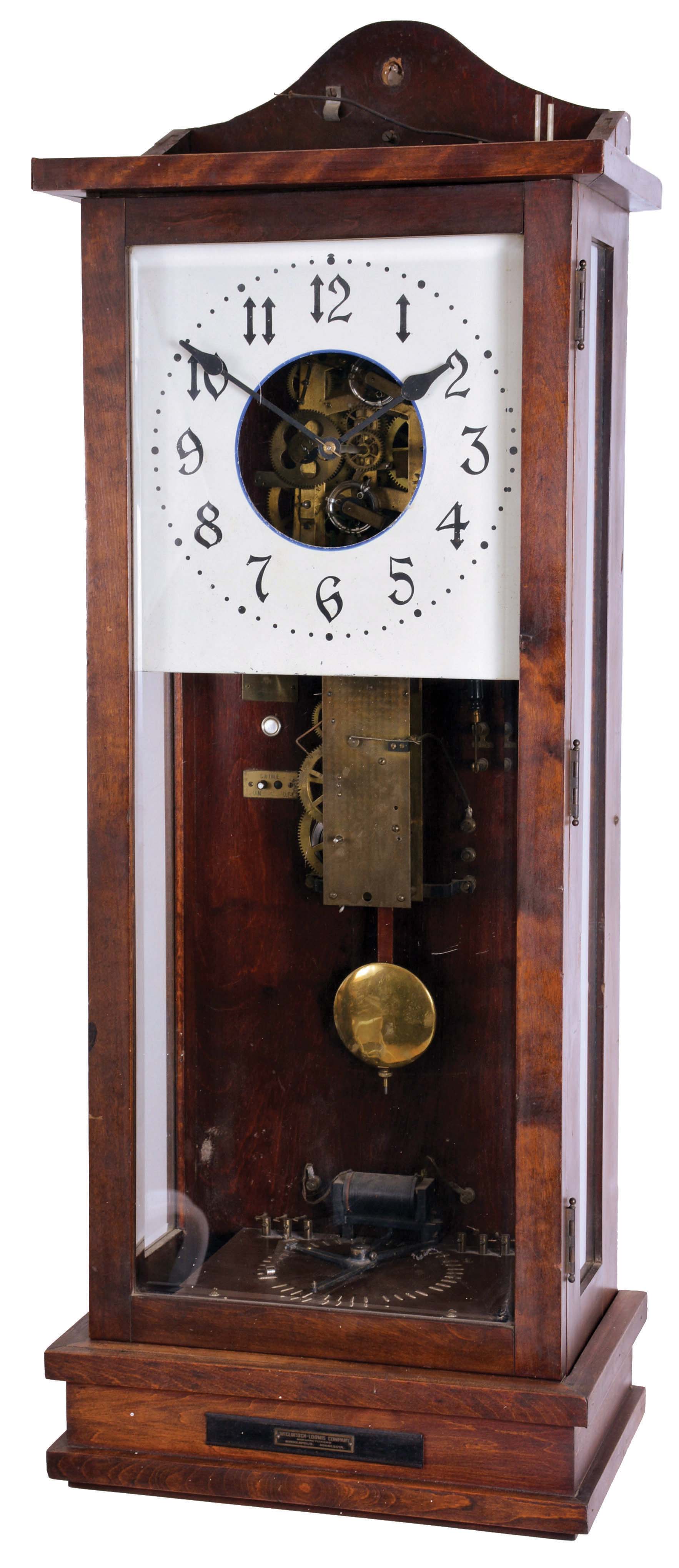 O.B. McClintock, Minneapolis, Minn., master clock, rectilinear birch case with beveled glass door and sides, Arabic numeral painted dial with open center providing a view of the modified Seth Thomas movement, separate count wheel chime movement mounted to case back, and with large clockwork motor in base driving a control arm for sending impulse to chime or bell hammers, case top with 14 output terminals — Antique Clocks Price Guide