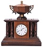 Automatic Memorandum Clock Co., London, "Davidson's Patent Automatic Memorandum Clock", 8 day time and reminder, spring driven, balance wheel movement in a walnut case with four full pillars and wooden urn on top. A time-only movement powers the clock and rotates a disk hidden within the urn. The disk has slots that correspond to different times of day. Memoranda, in the form of small bone tablets upon which one can write a few words, are placed within the slots. At the assigned time, a tablet falls through the slot, tips a brass tray, and triggers the battery powered alarm bell located in the base. The alarm would continue to sound until the tablet was removed.