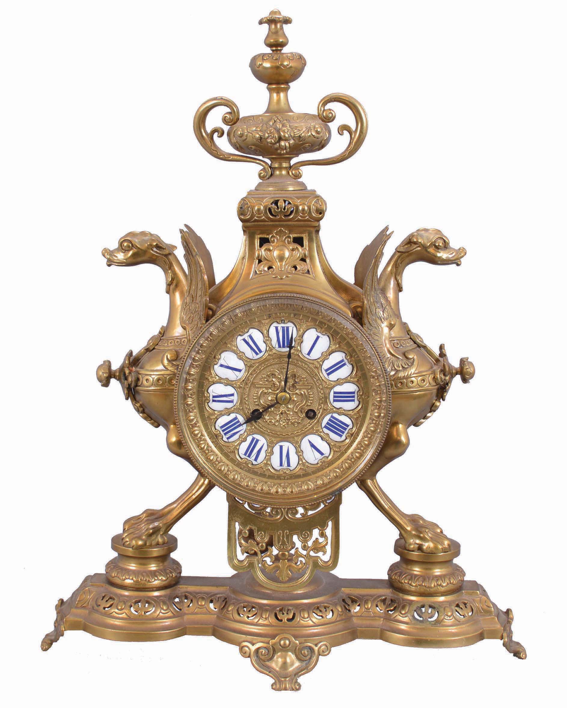 France, figural brass mantel clock, 8 day, time and strike on a pierced base with two short pillars supporting winged griffon figures in profile flanking a central cylinder holding an ornate brass dial with blued steel hands and white enameled cartouche numerals in blue, surmounted by a decorative urn. The pendule de Paris movement with partially exposed pendulum is stamped "CHLES MT". — Antique Clocks Price Guide