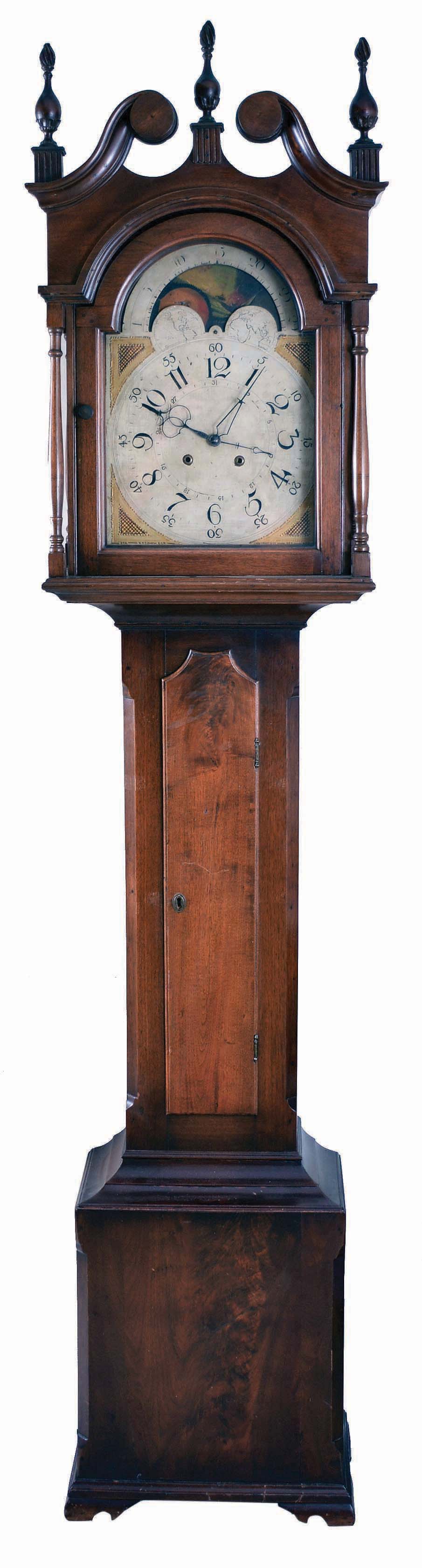 Pennsylvania, tall case clock, 30 hour, time and bell strike, single weight driven movement in a walnut case with broken arch top, three wooden flame finials, four turned columns at bonnet corners, over cove molded trunk with shaped door top, and crotch walnut base resting on ogee bracket feet. The painted metal dial retains its originalpaper label, "CURTIS' MANUFACTORY FOR PATTON & JONES, PHILADELPHIA" and has calendar hand off center arbor, moon phase with interesting burning ship scene. — Antique Clocks Price Guide