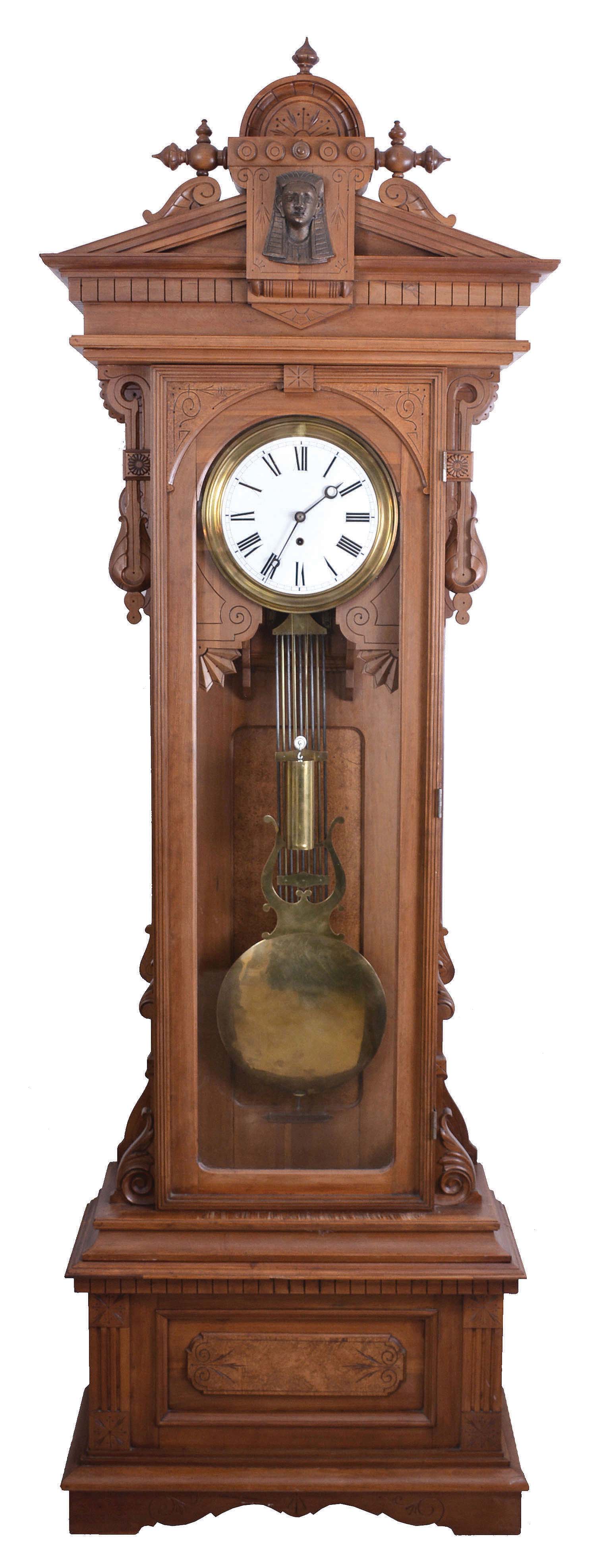 Wm L. Gilbert, Winsted, Conn., "Standing Regulator No. 8" 8 day, time only, weight driven brass movement with Graham deadbeat escapement, maintaining power, gridiron pendulum and sweep seconds in a carved cherry case, the crest with central sphinx head ornament, and Roman numeral white enamel dial. — Antique Clocks Price Guide