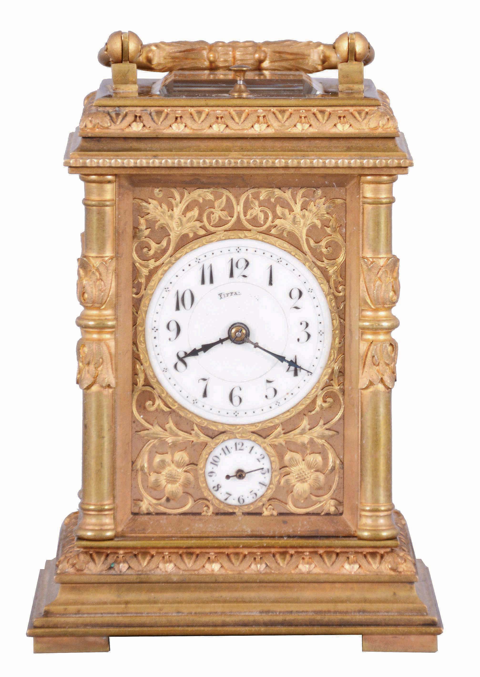 France, for Tiffany & Co., a Pillars style, petit sonnerie striking carriage clock with repeat, the glazed, gilt case with bright and matte surfaces, the base and cornice with cavetto and egg and dart moldings, the corners with acanthus decorated columns, and carrying handle also with foliate ornament, Arabic numeral white enamel dial with fretted, matte gilt foliate mask against a bright gilt background, blued steel distaff hands, 8 day time, strike, and alarm movement with lever platform, sounding petit sonnerie quarters in passing, with grand sonnerie repeating on demand, the base with strike/ silent lever — Antique Clocks Price Guide