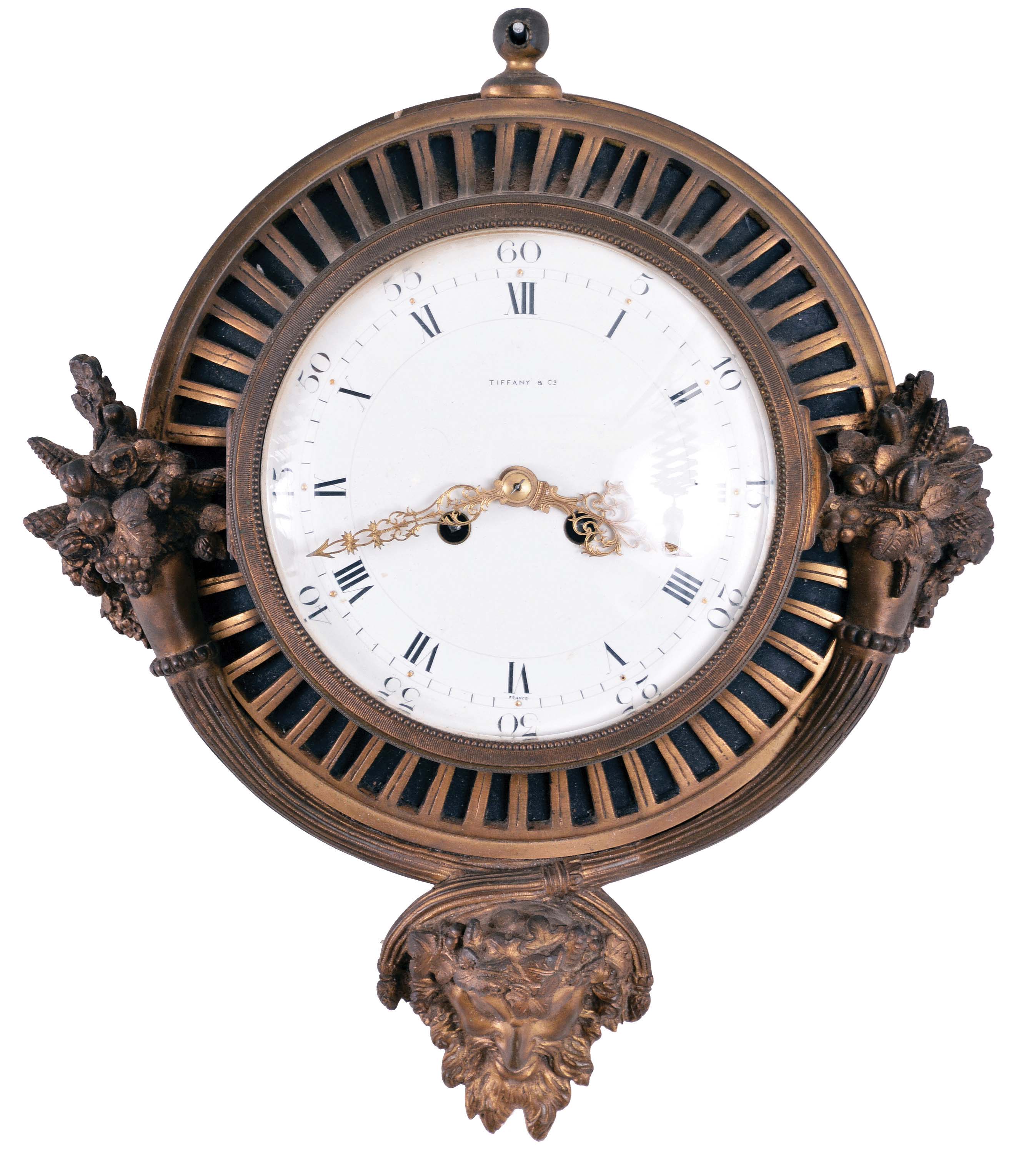 Gilt Brass Cartel Wall Clock with 7.5 inch porcelain roman numeral dial marked "Tiffany" and "France", pierced gilt hands all set in a cast brass fluted case with overflowing cornucopias of flowers and fruit at the sides and a mythological god of plenty mask at the bottom, eight-day French spring powered movement with lever platform escapement and bell strike. — Antique Clocks Price Guide