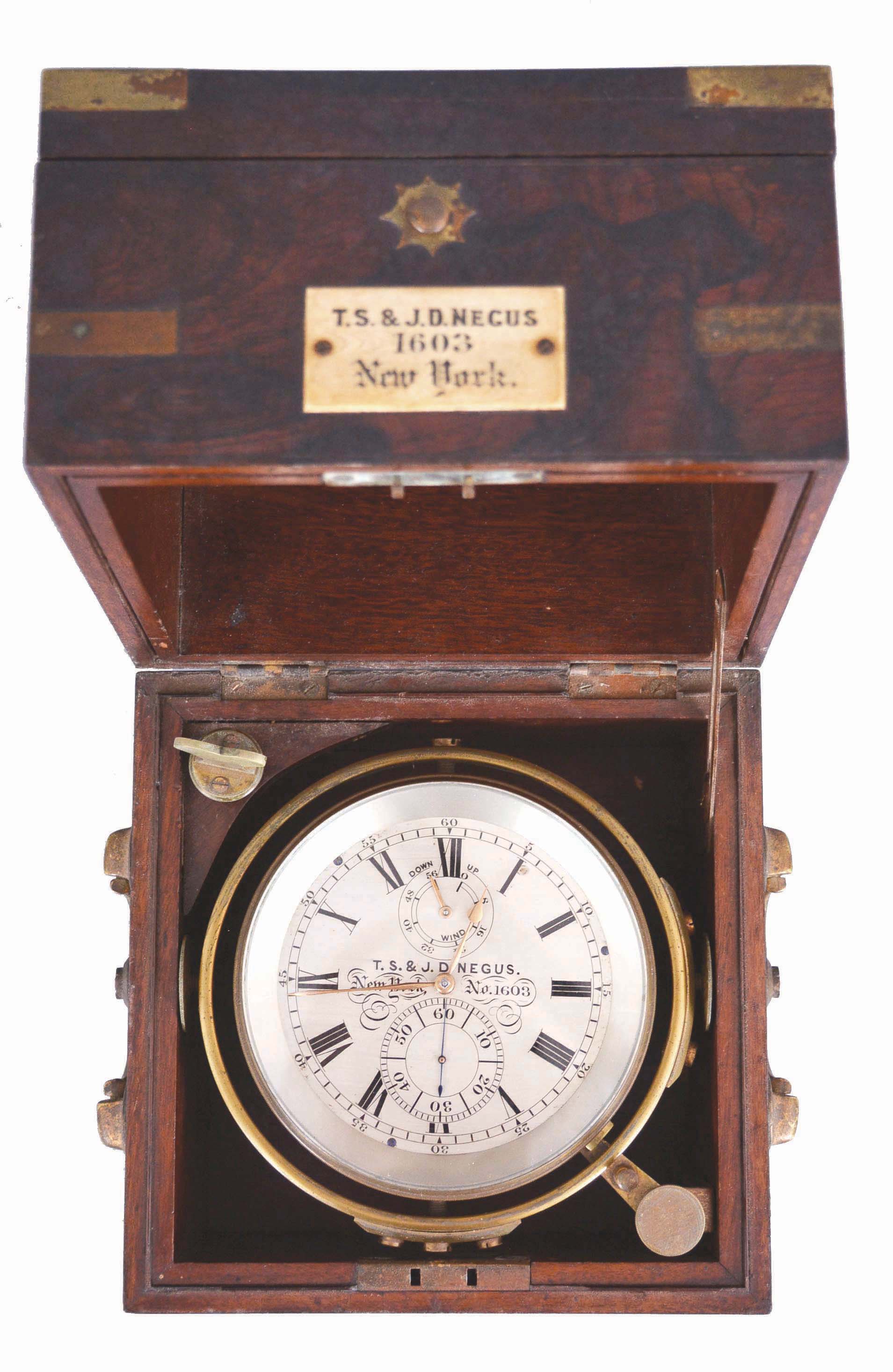 T.S. and J.D. Negus, New York, a good two day marine chronometer with original box, 11 jewel, free sprung fusee movement with Earnshaw's spring detent, cut, bimetallic chronometer balance with blued helical spring, and diamond endstone, signed Roman numeral silvered dial with wind indicator, gold spade and poker hands, contained in a lacquered brass bowl with gimbals, and mounted in a mahogany and rosewood veneer box with brass furniture, and plaque engraved "T.S. & J.D. Negus 1603 New York", the box also with rating certificate from L. A. Karcher & Co., Boston — Antique Clocks Price Guide