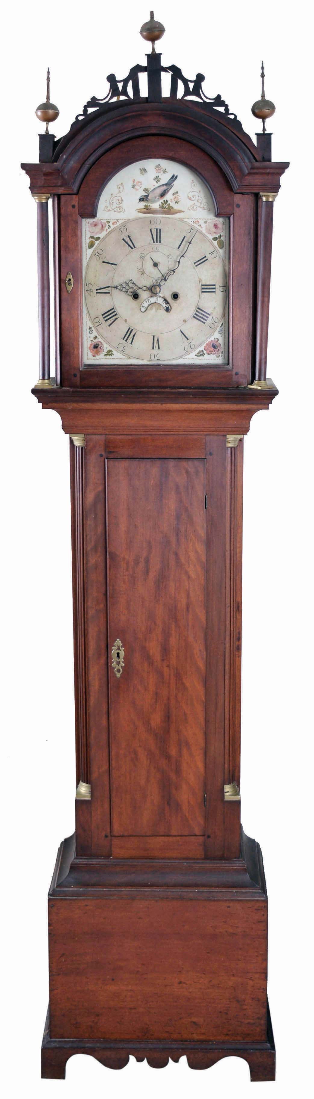 Timothy Chandler, Concord, New Hampshire, Roxbury style tall case clock, 8 day, time and strike, weight driven movement in a red stained yellow birch case with fret work top, three brass finials, turned columns flanking hood, fluted quarter columns with brass capitals flanking trunk door on base with nicely cutout skirt and straight bracket feet. The painted metal dial has floral painted spandrels, bird in arch, seconds bit and calendar wheel. — Antique Clocks Price Guide