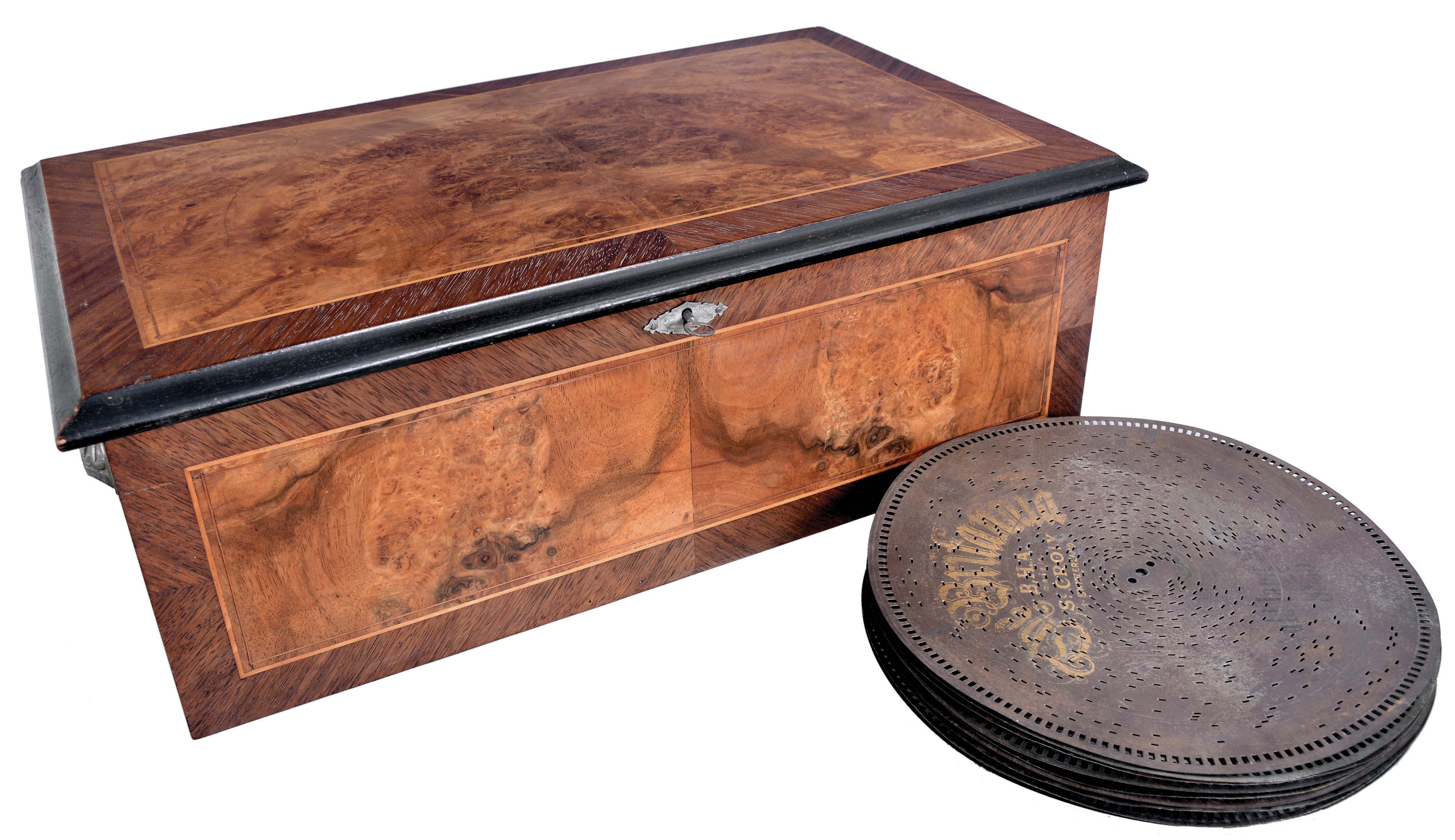 B.H.A., St. Croix, Switzerland, "The Brittania" disc music box with 5 inch comb having 57 teeth, playing 12 inch diameter discs, in wood case with matched mahogany and burled walnut veneer and banded inlay, the underside of the lid featuring the manufacturer and model name along with polychrome images symbolizing Great Britain 11 (Eleven) discs included, most printed with the Britannia logo. Song titles include: "The Holy City", "Annie Laurie", "Rock of Ages", "Onward Christian Soldier", and others. — Antique Clocks Price Guide