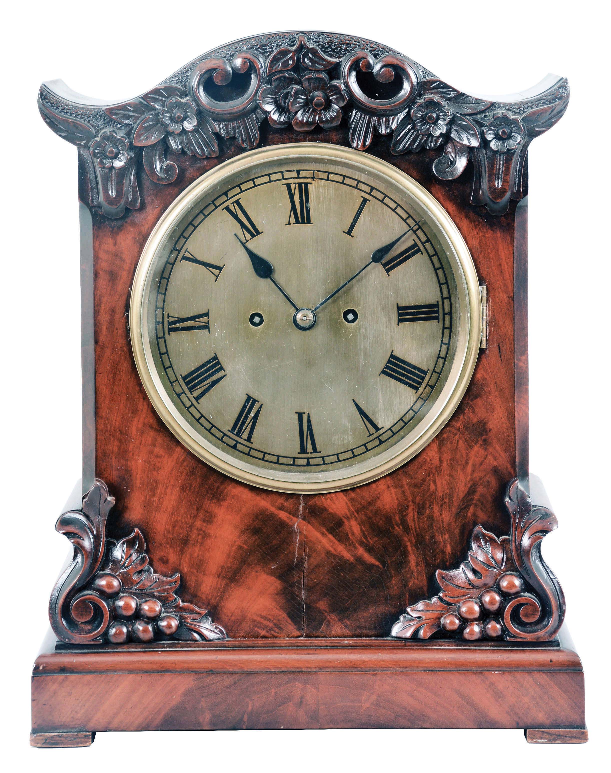 English Victorian Table Clock, with engraved brass roman numeral dial and blued spade hands, brass bezel and beveled glass, figured mahogany case with carved serpentine top featuring scrolls, flowers and leafage, chamfered corners flanking the dial, ogee-shaped buttresses with oak leaves and acorns on the facade, pierced sound vents on the sides, all resting on a molded base with pad feet, eight day, brass fusee spring-powered movement with recoil escapement and hour strike on a gong. — Antique Clocks Price Guide