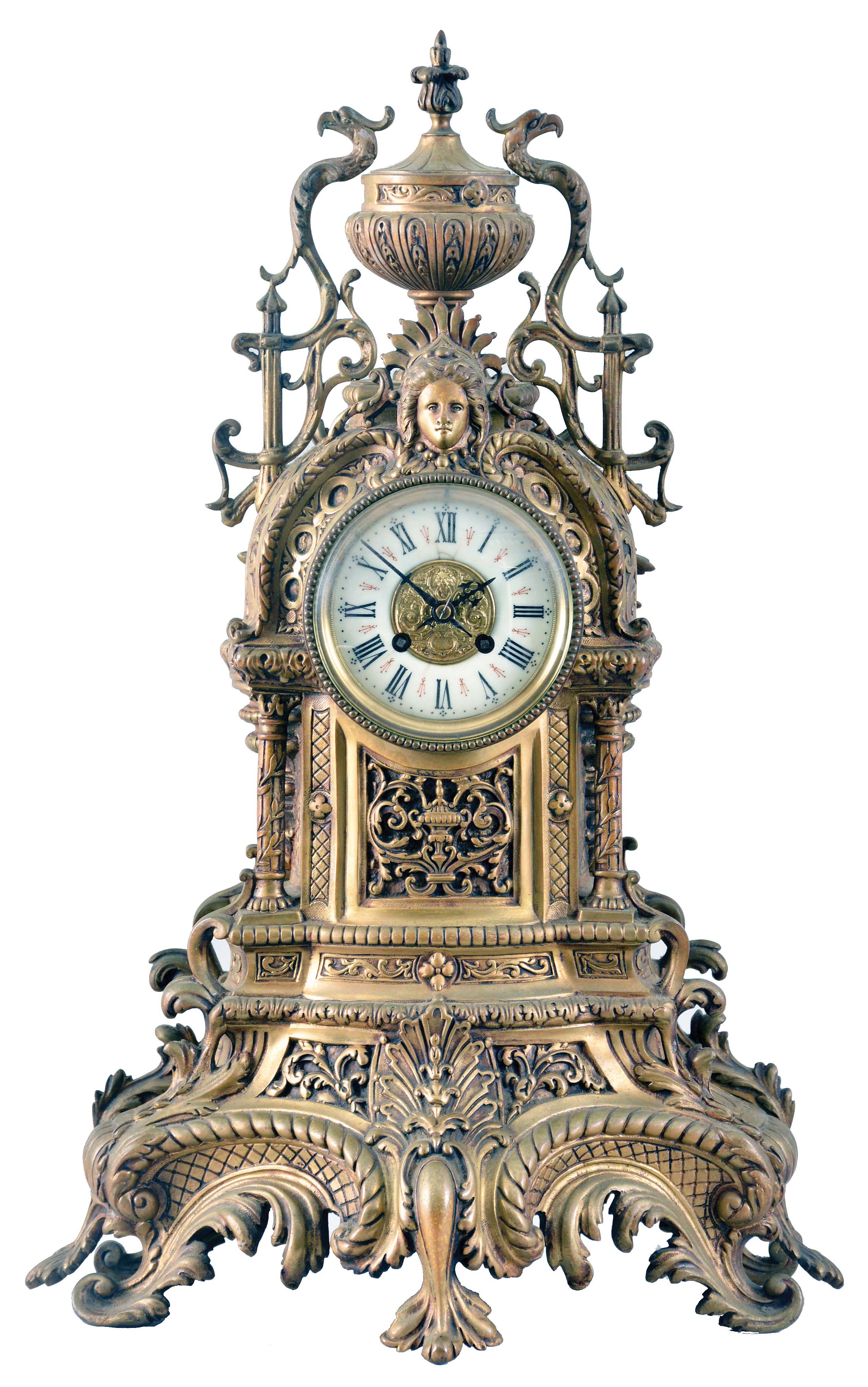 France, Mantel Clock with porcelain roman numeral dial and decorative cast center, blued-steel hands, complicated classical-styled cast brass case with urn finial at the top flanked by griffins, a female goddess of the sun life mask surmounting the dial, four fluted columns supporting the whole and a leaf and scroll base with cross hatching and four scroll-leafed feet, round brass French eight day movement with rack hour striking on a gong and pendulum. — Antique Clocks Price Guide