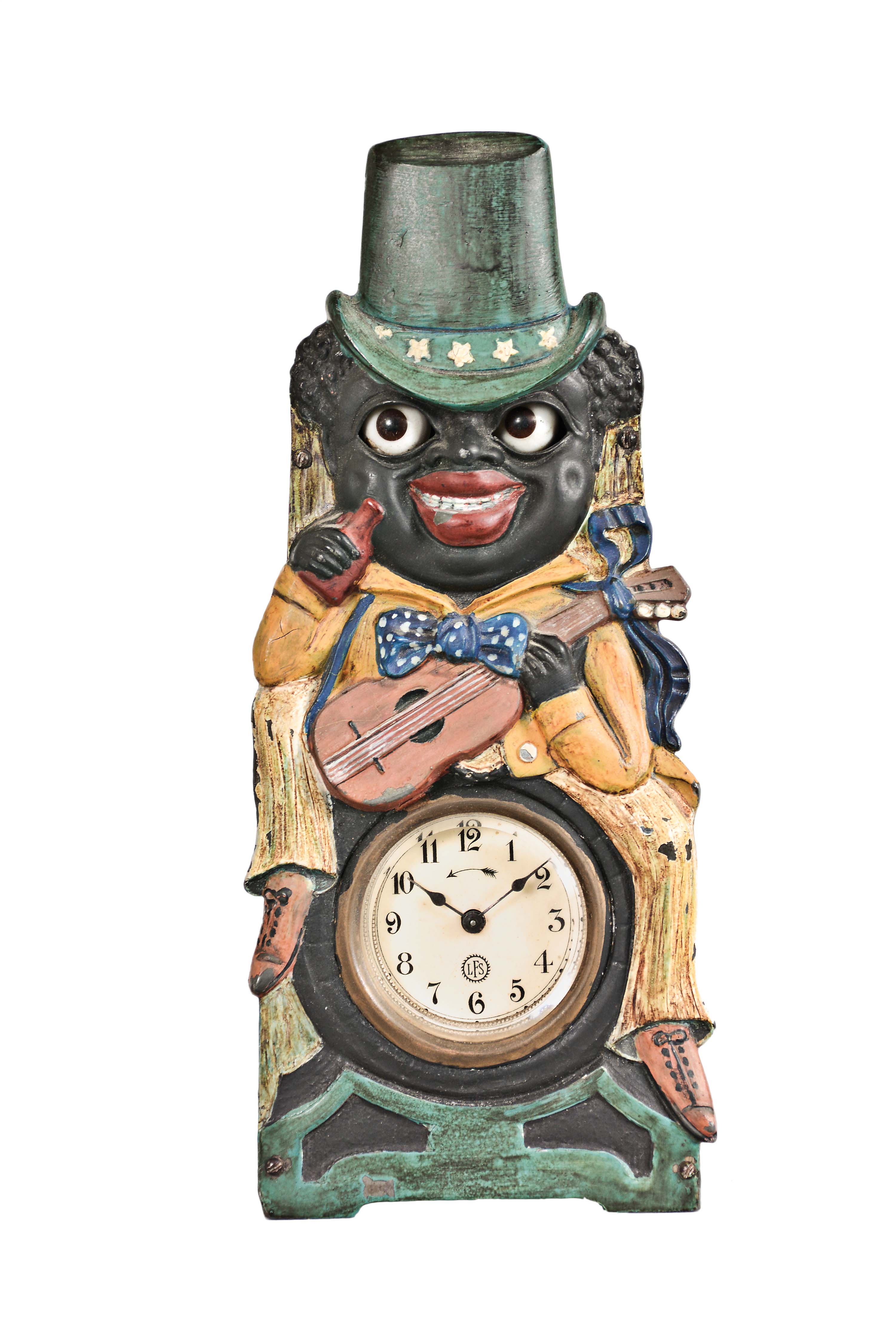 Lorenz Furtwangler & Sohne a "Minstrel" moving eye novelty clock, the front cast in the form of an early 20th century stereotype of the strumming, drinking African- American, his clothing brightly painted, and his large, glass eyes, connected to the pallet arbor, moving to and fro as the clock runs, signed, Arabic numeral celluloid dial, blued steel spade hands, thirty hour timepiece movement — Antique Clocks Price Guide