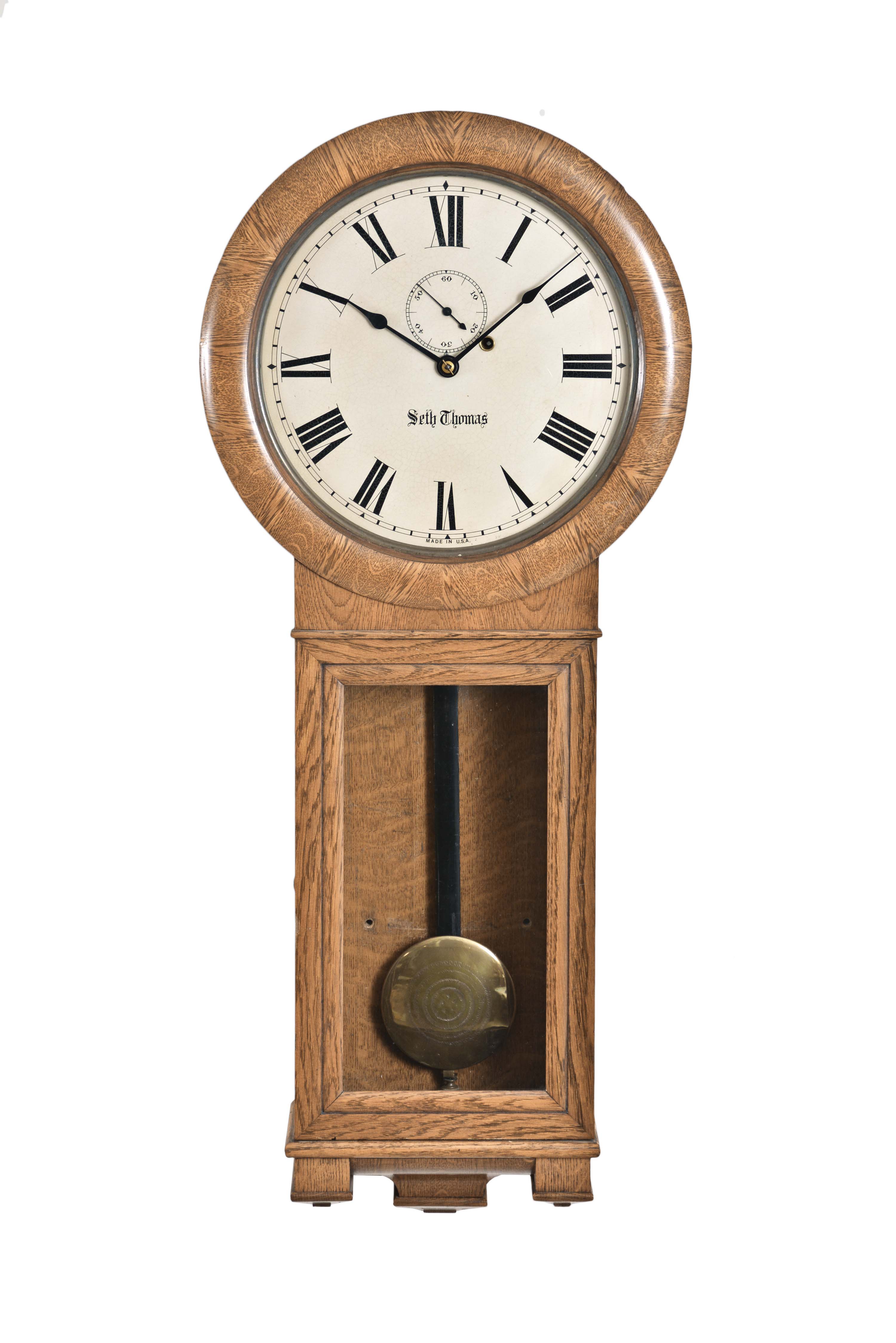 Seth Thomas Clock Co., Thomaston, Conn., "Regulator No. 2" in an oak case with veneered dial bezel over the 12-inch dial with seconds and marked "Seth Thomas", the lower glazed section for access to weight and pendulum locks with the winding key, three-part pedestal below, eight day brass time only movement with dead beat escapement, maintaining power, lantern pinions, mounted to an iron frame attached to backboard, cylindrical brass weight and pendulum with flat painted wooden rod and decorated brass-faced bob. — Antique Clocks Price Guide
