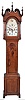 Pennsylvania tall clock, 30 hour, time and strike, weight driven brass movement in a walnut case with broken arch top, flame rosettes protruding about 1.5" from end of neck, three wooden finials on wooden chimneys, four shaped full columns flanking hood, paneled plinth, trunk door flanked by quarter columns is made with unusual large knot on ogee bracket base with quarter columns. The painted metal dial has calendar disc and floral and grape painted decorations.