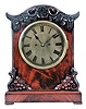 English Victorian Table Clock, with engraved brass roman numeral dial and blued spade hands, brass bezel and beveled glass, figured mahogany case with carved serpentine top featuring scrolls, flowers and leafage, chamfered corners flanking the dial, ogee-shaped buttresses with oak leaves and acorns on the facade, pierced sound vents on the sides, all resting on a molded base with pad feet, eight day, brass fusee spring-powered movement with recoil escapement and hour strike on a gong.