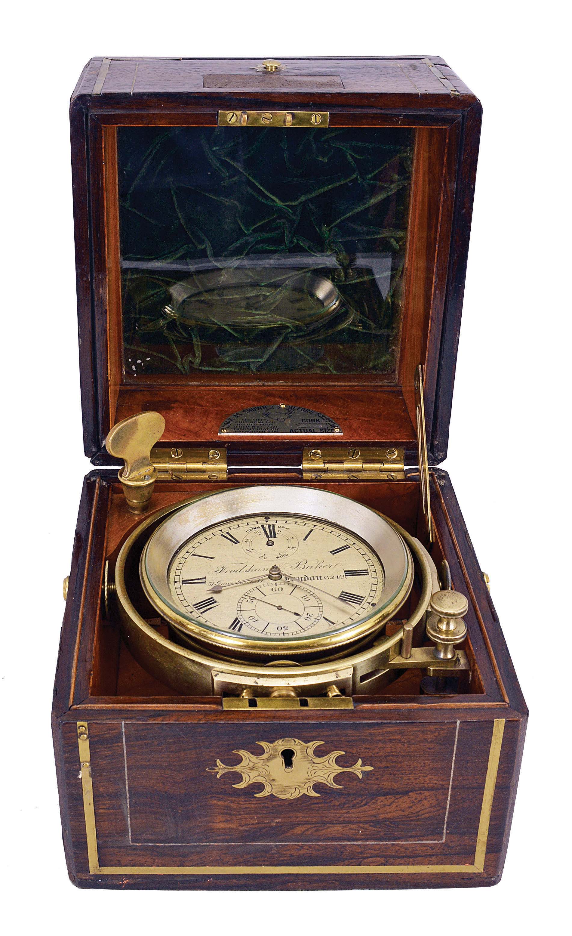 Frodsham and Baker, 31 Gracechurch St., London, two day marine chronometer with Molyneux's auxiliary compensation, 11 jewel fusee movement with Earnshaw's escapement, and freesprung, cut bimetallic balance with diamond endstone, blued steel helical balance spring and jewelled auxiliary compensation, Roman numeral silvered dial with wind indicator and gold spade and poker hands, contained in a brass bowl, and mounted in a very decorative, brass inlaid, rosewood veneered mahogany box with gimbals and lacquered brass furniture — Antique Clocks Price Guide