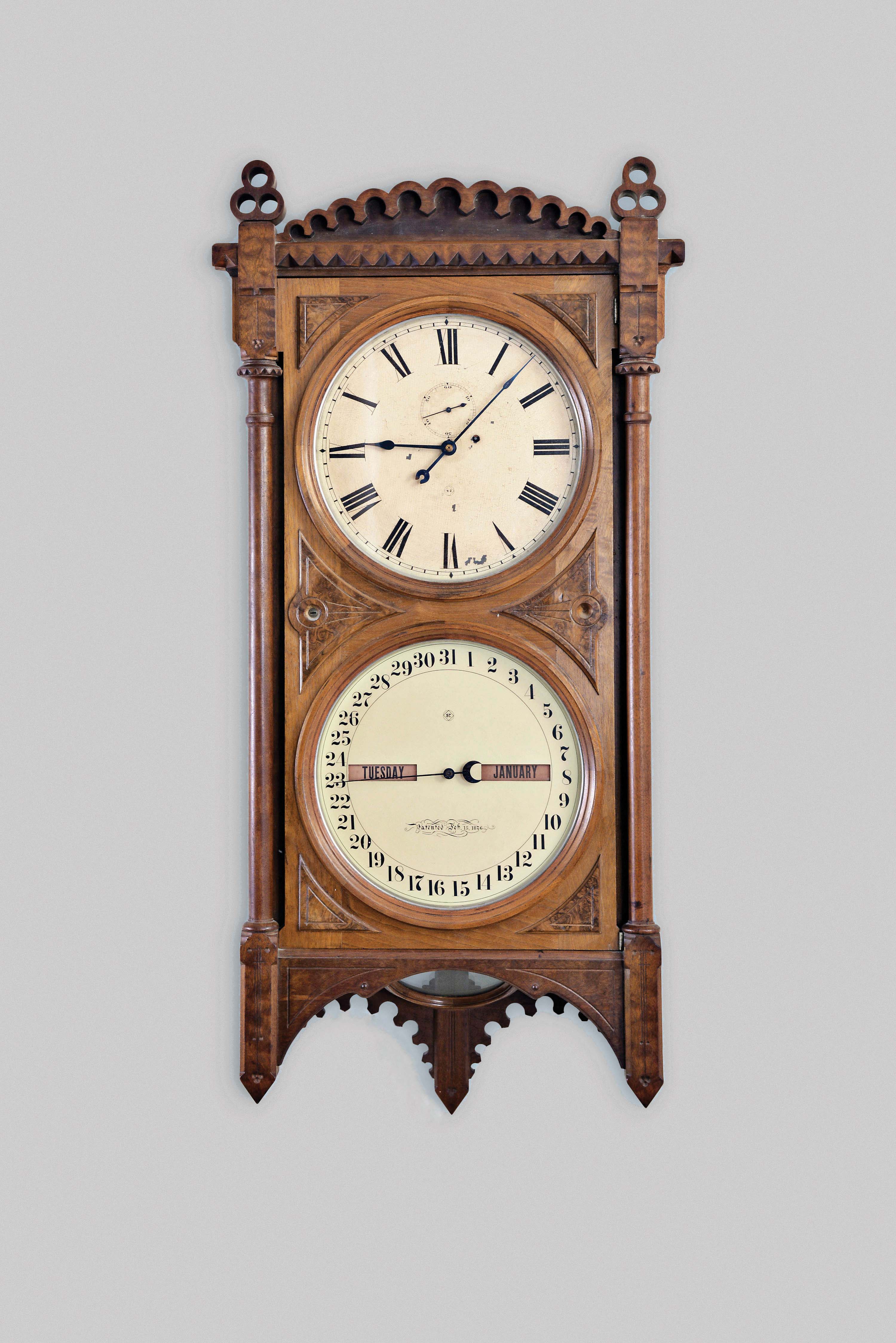 Seth Thomas Clock Co., Thomaston, Conn., "Office Calendar No. 5" wall clock, 8 day, weight driven movement with perpetual calendar in a walnut case with six burl spandrels on front door and lenticular aperture for pendulum bob and painted metal dials — Antique Clocks Price Guide