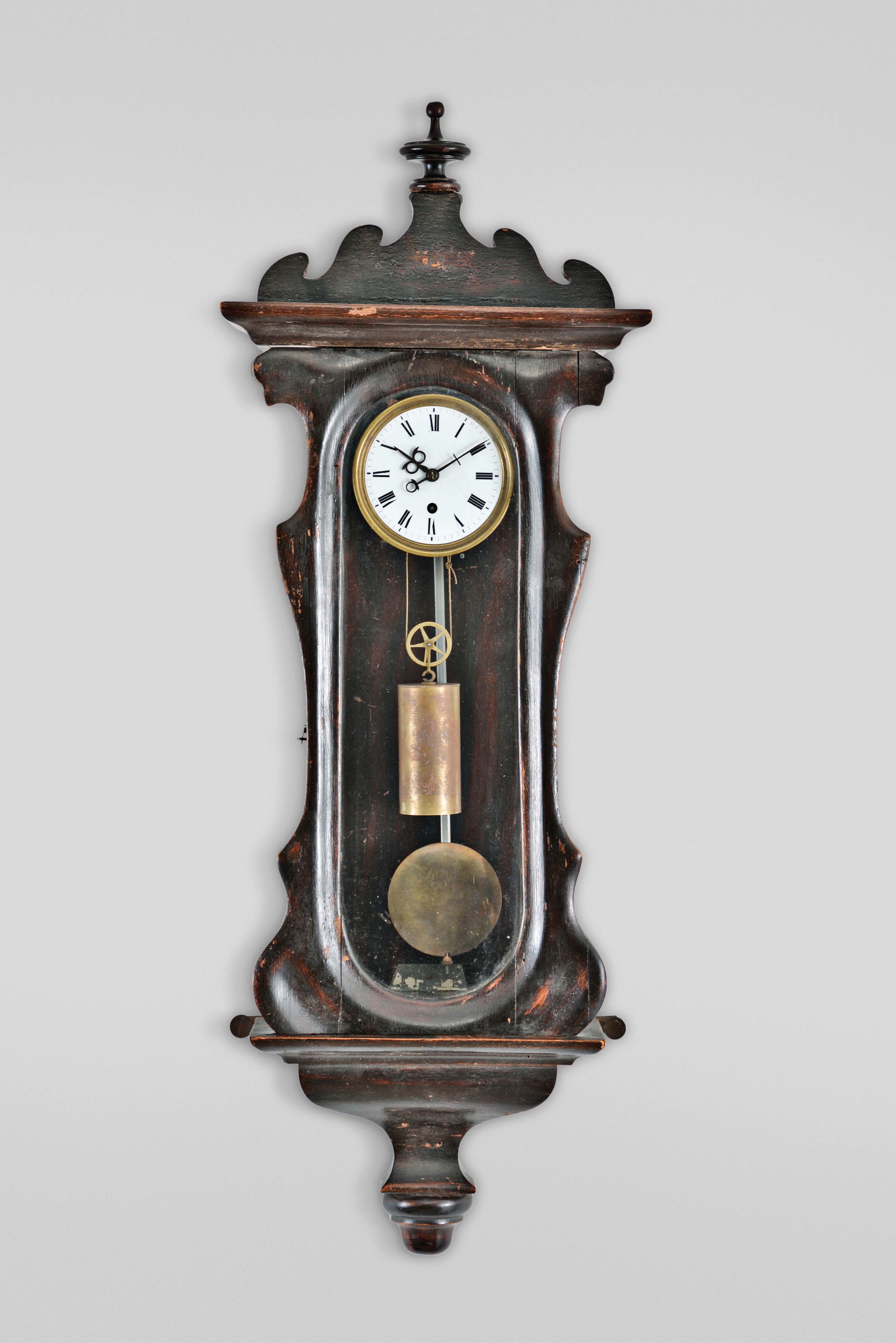 Austria, a miniature weight driven Vienna timepiece, rosewood grained softwood case with serpentine door, deeply molded bottom bracket with turned drop, ogee molded top and bottom, and removable scrolled crest with turned finial, Roman numeral white enamel dial, pierced, blued steel Vienna style hands, 30 hour, weight driven timepiece movement with recoil escapement and silk thread suspension, 5 spoke pulley, and pendulum with brass bob and steel rod — Antique Clocks Price Guide