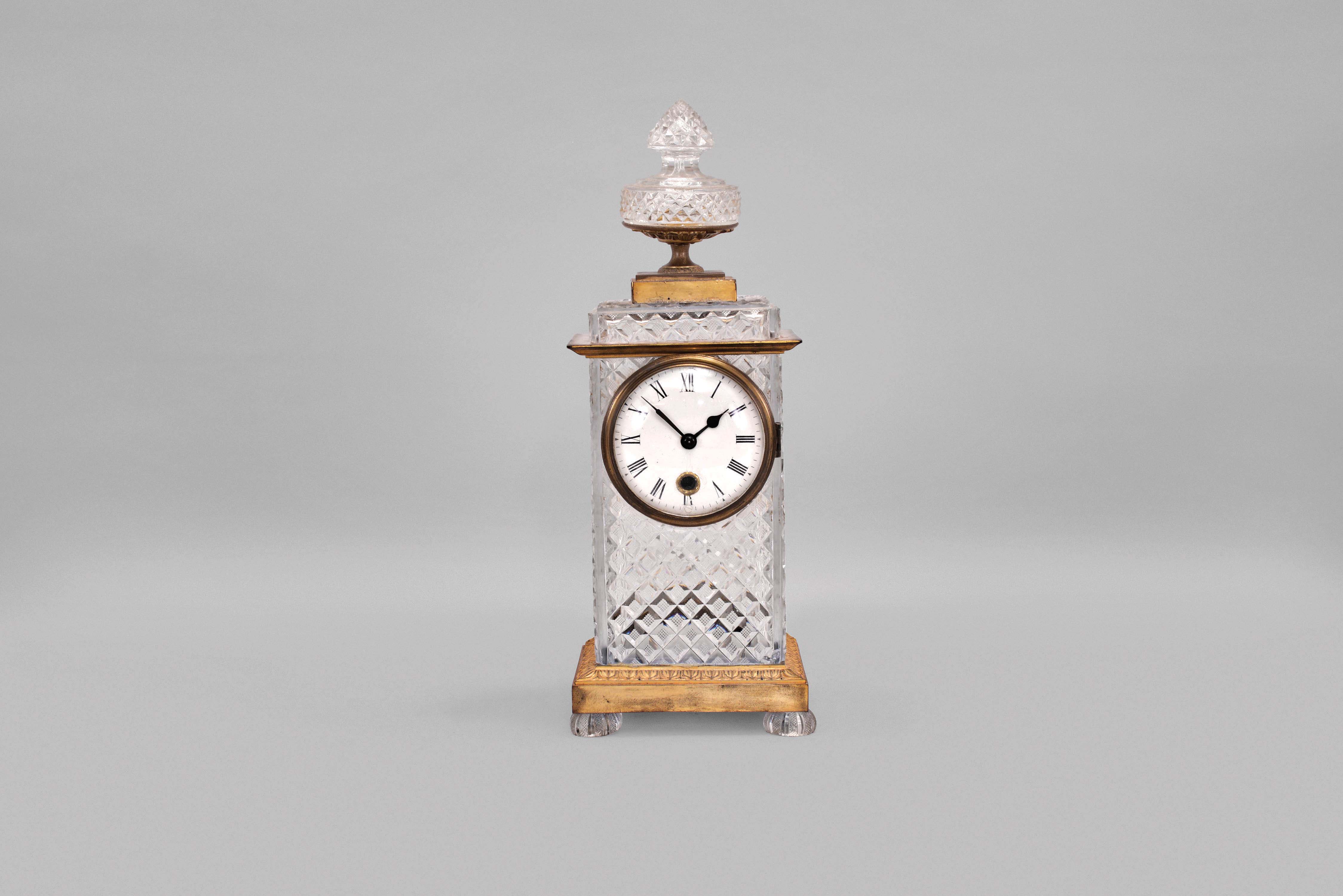France, an unusual gilt bronze and cut glass mantel clock, possibly Baccart, the rectilinear case with egg and dart molded base on cut, flattened ball feet, cyma recta molded cornice, and surmounted by a gilt plinth with acanthus decorated support for the cut glass finial, the case with crosshatched, diamond cutting, Roman numeral white enamel dial with brass bezel, blued steel spade and poker hands, and 8 day, timepiece movement — Antique Clocks Price Guide