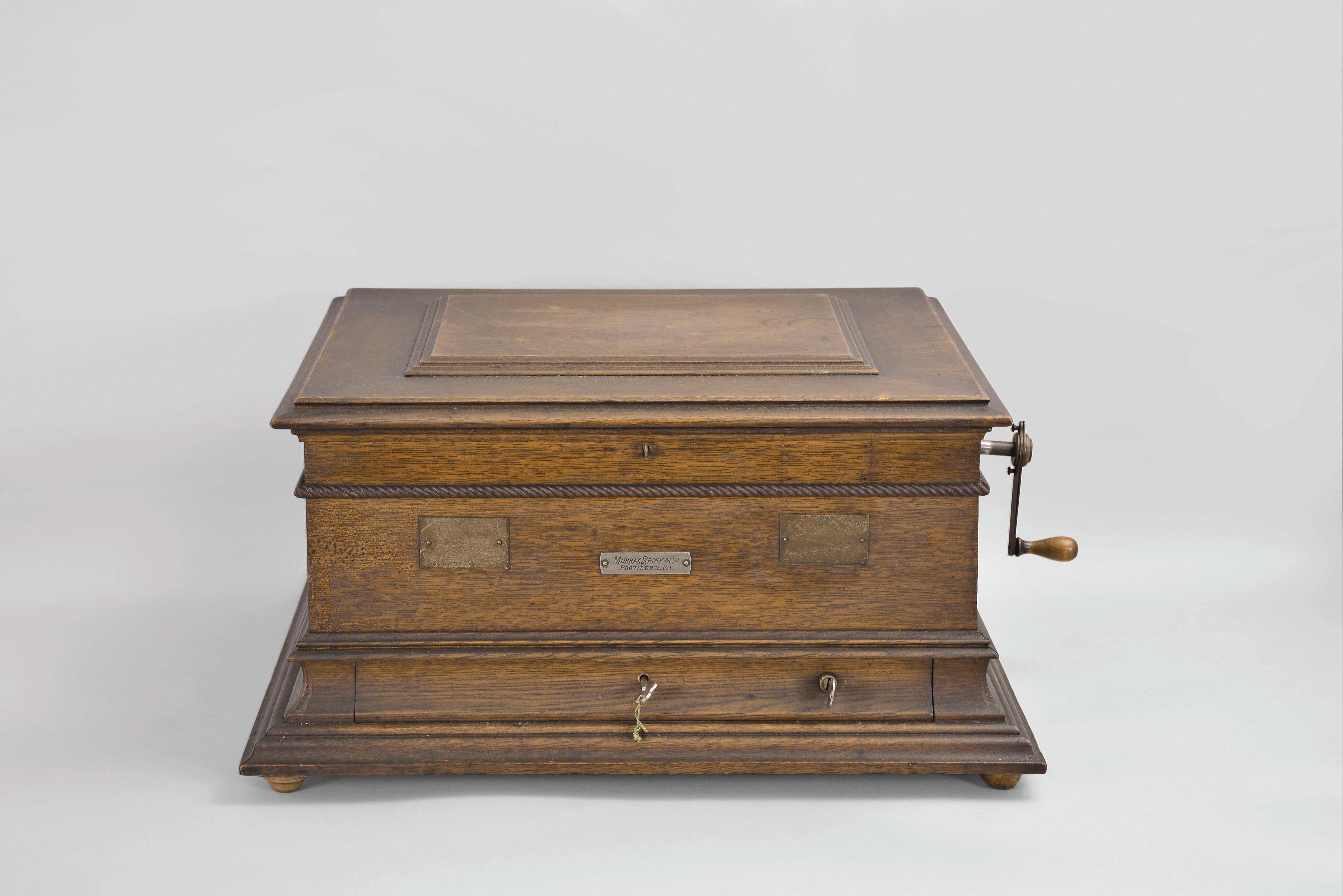 Regina Musical Box Co., Rahway, N.J., "Style 11a" 15.5 inch double comb music box with 10 discs, oak case with stepped ogee base and locking drawer, rope molding, stepped, molded lid, the inside with music-themed Regina lithograph, front metal plate reading "Murray, Spink Co. / Providence, R.I.". — Antique Clocks Price Guide