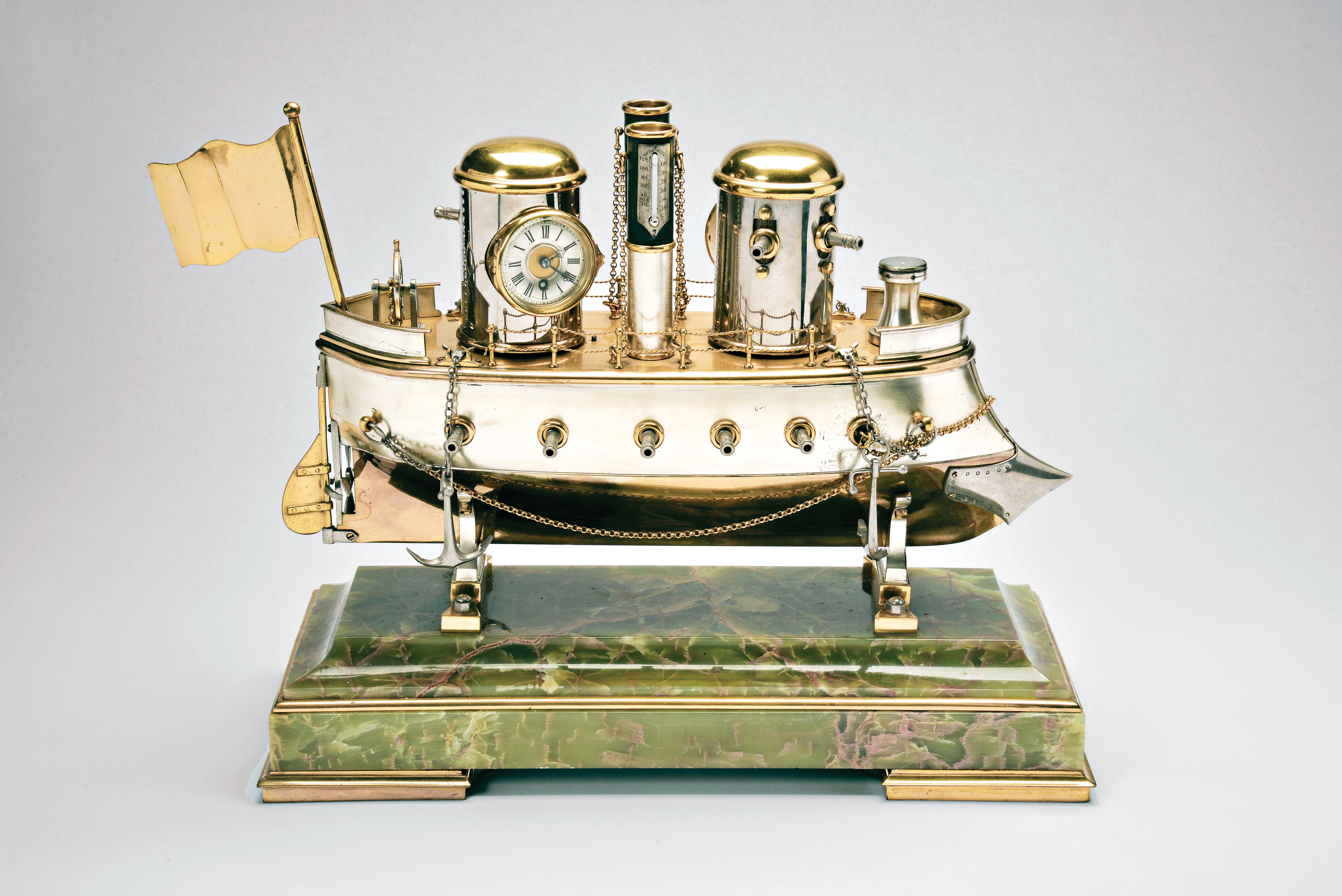France, possibly Andre Romain Guilmet, a rare silvered and gilt brass, automated, battleship form compendium, the vessel bow with ram, fourteen cannon, and four anchors, the gilt deck with capstan containing a compass, two revolving gun turrets, one having an 11 jewel lever timepiece, with roman numeral silvered dial and blued steel trefoil hands, the other with aneroid barometer, also with silvered dial, the stacks with mounted Fahrenheit and Centigrade thermometers, the stern with ships wheel and flag, above the articulated rudder and revolving propeller, a movement concealed in the ship's hull providing power to the turrets and propeller, which may be started and stopped at will by a projection attached to the rudder, all mounted to a rectangular, molded, green onyx base with gilt trim and feet — Antique Clocks Price Guide