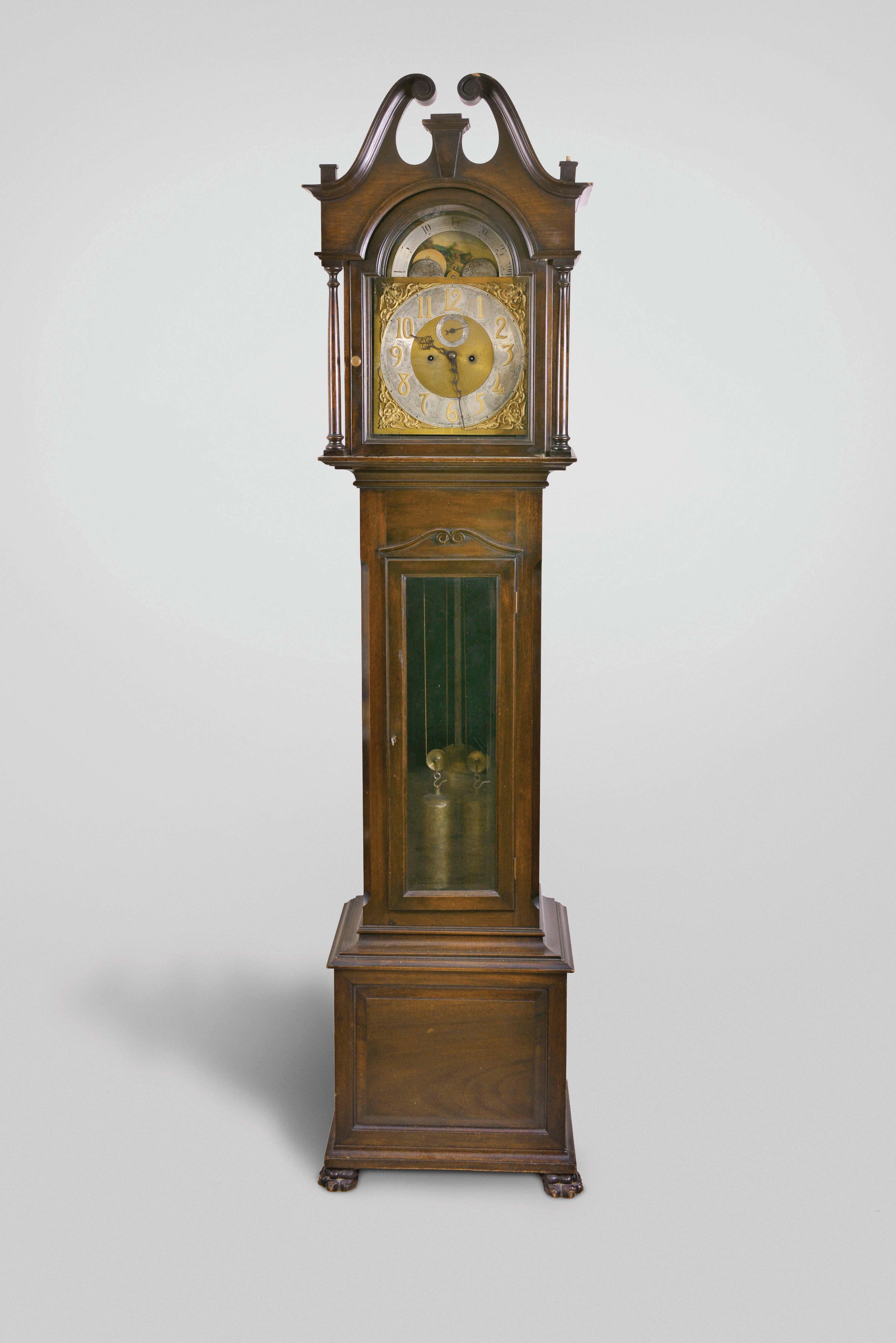 Germany, tall clock, 8 day, time and strike, brass weight driven movement in a mahogany case with broken arch top, full turned columns flanking hood door, pierced fretwork on sides, beveled trunk door glass and paw feet. The brass dial has silvered chapter ring with applied brass numerals, moon phase, and applied brass spandrels. — Antique Clocks Price Guide