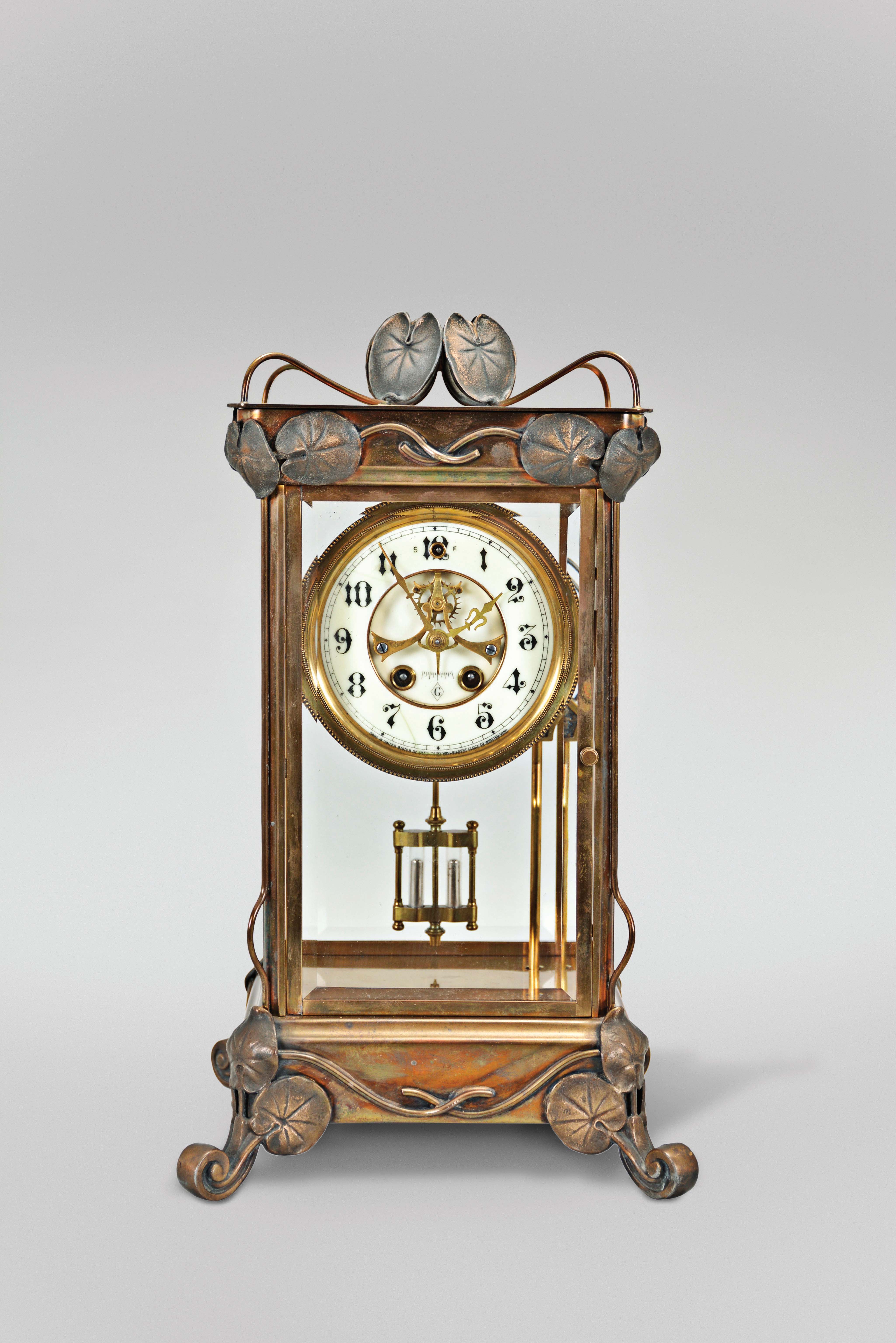 William L. Gilbert Clock Co., Winsted, Conn., "Ruskin" crystal regulator shelf clock with a spring driven, 8 day, time and strike visible escapement movement with patent self adjusting beat in a polished brass case. The hour strike is on a cathedral gong and the half hour strike on a separate cup bell. — Antique Clocks Price Guide