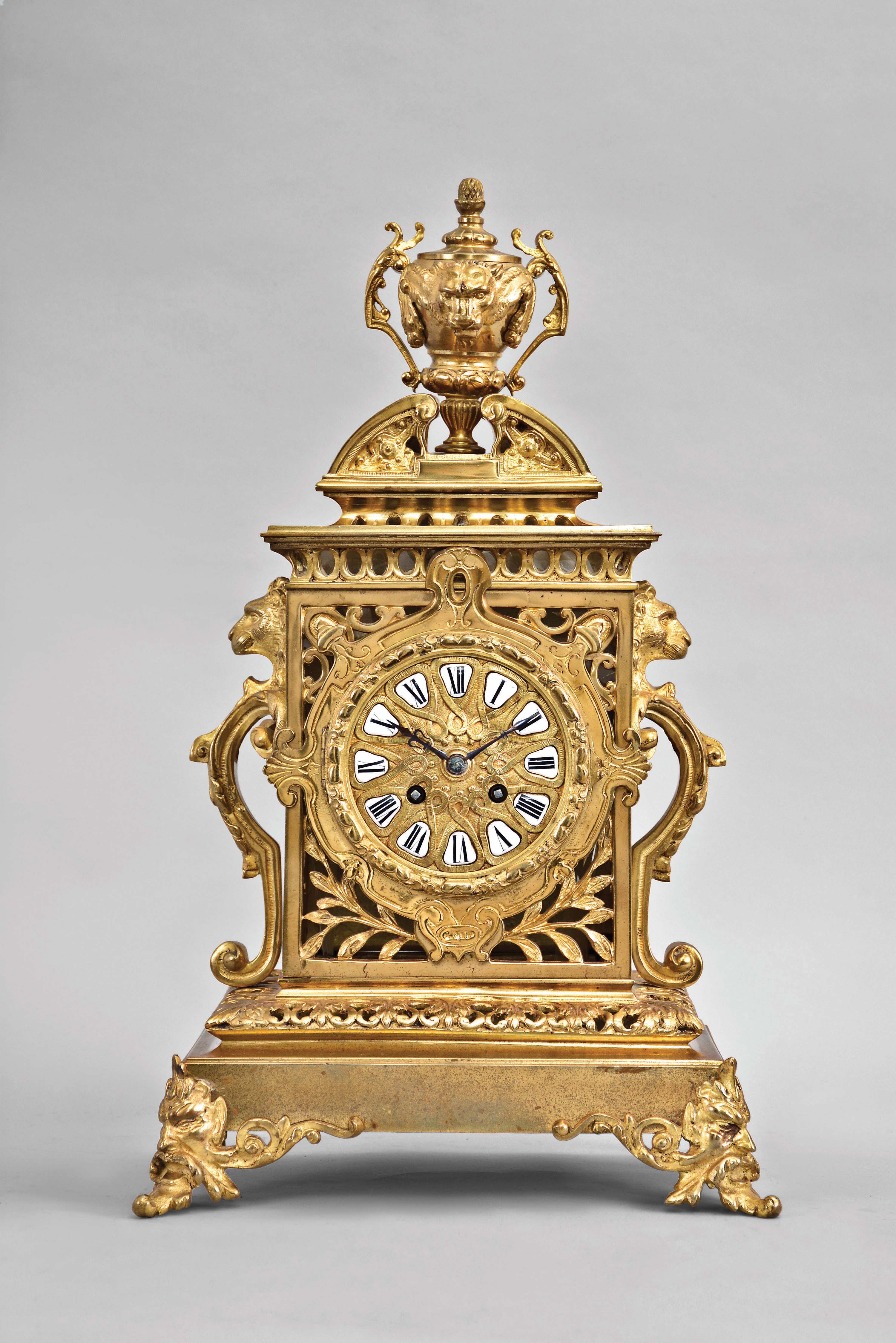 France, mantel clock, 8 day, time and strike, spring driven pendule de Paris movement in a cast brass Renaissance Revival case with gilt accents, front feet in the form of foliate faces, lion masks on either side and on top urn finial, dial with white enamel cartouches and blued steel hands. — Antique Clocks Price Guide