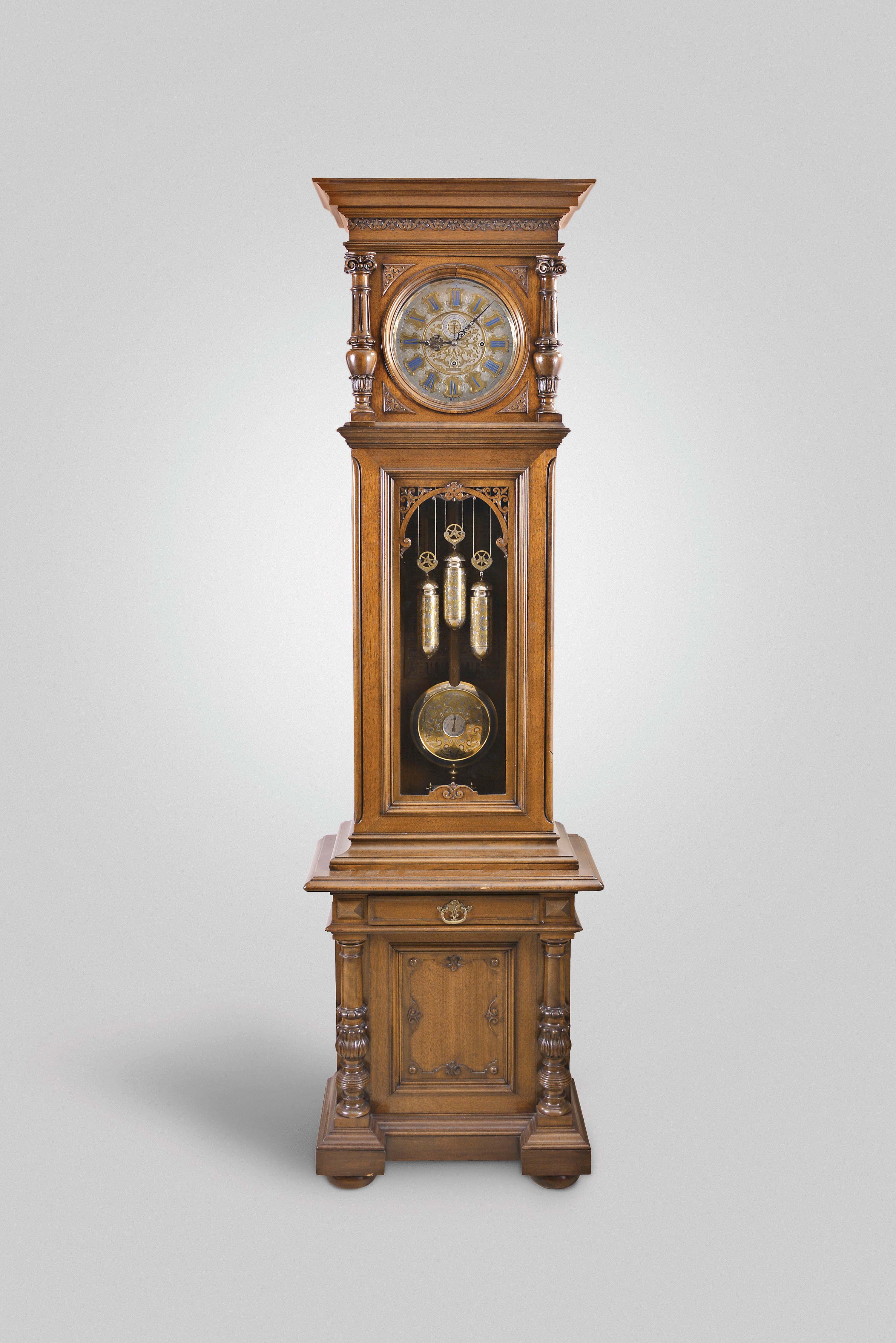 Anton Jezek, Wien, Austria, 30 day, time, strike & grande sonnerie, weight driven movement in a two piece carved walnut case with carved and turned half columns flanking dial, carved fleur-de-lis style trim over trunk door glass over a base with a single drawer, cabinet and two carved and turned 3/4 columns resting on bun feet. The intricately engraved nickel plated dial has blue numerals on raised engraved brass plaques with maker's signature "Ant. Jezek" and matching pendulum disc and weights. — Antique Clocks Price Guide