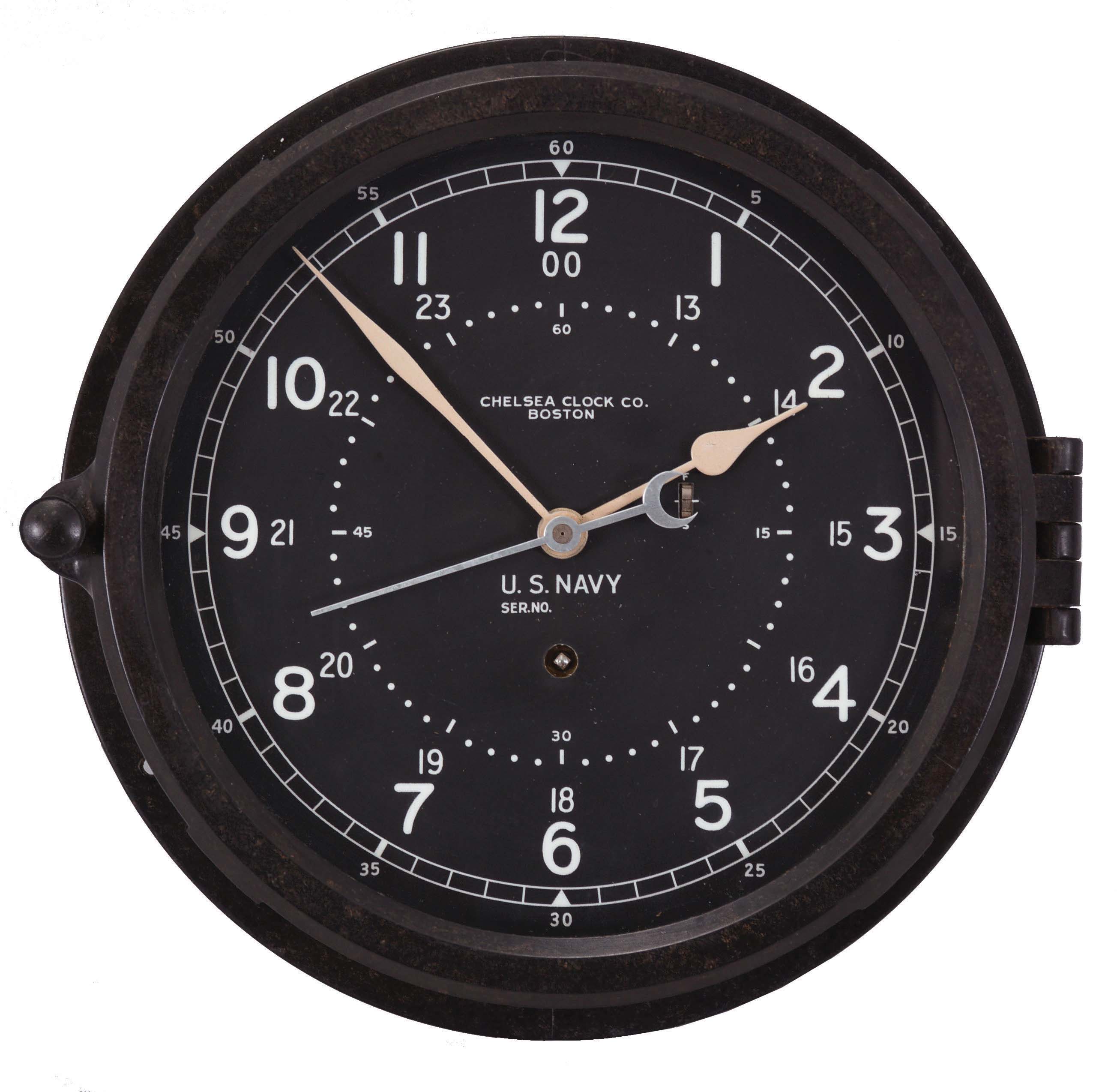 Chelsea Clock Co., Boston, Mass., "12E Deck & Engine Room Clock", 8 day, time only, spring driven movement with jeweled lever escapement and center seconds in a black phenolic case with hinged bezel, 8.5 inch black dial signed by the maker and with "U.S. Navy", 12 and 24 hour markers, white spade hands, movement serial number 785464, c1974. — Antique Clocks Price Guide