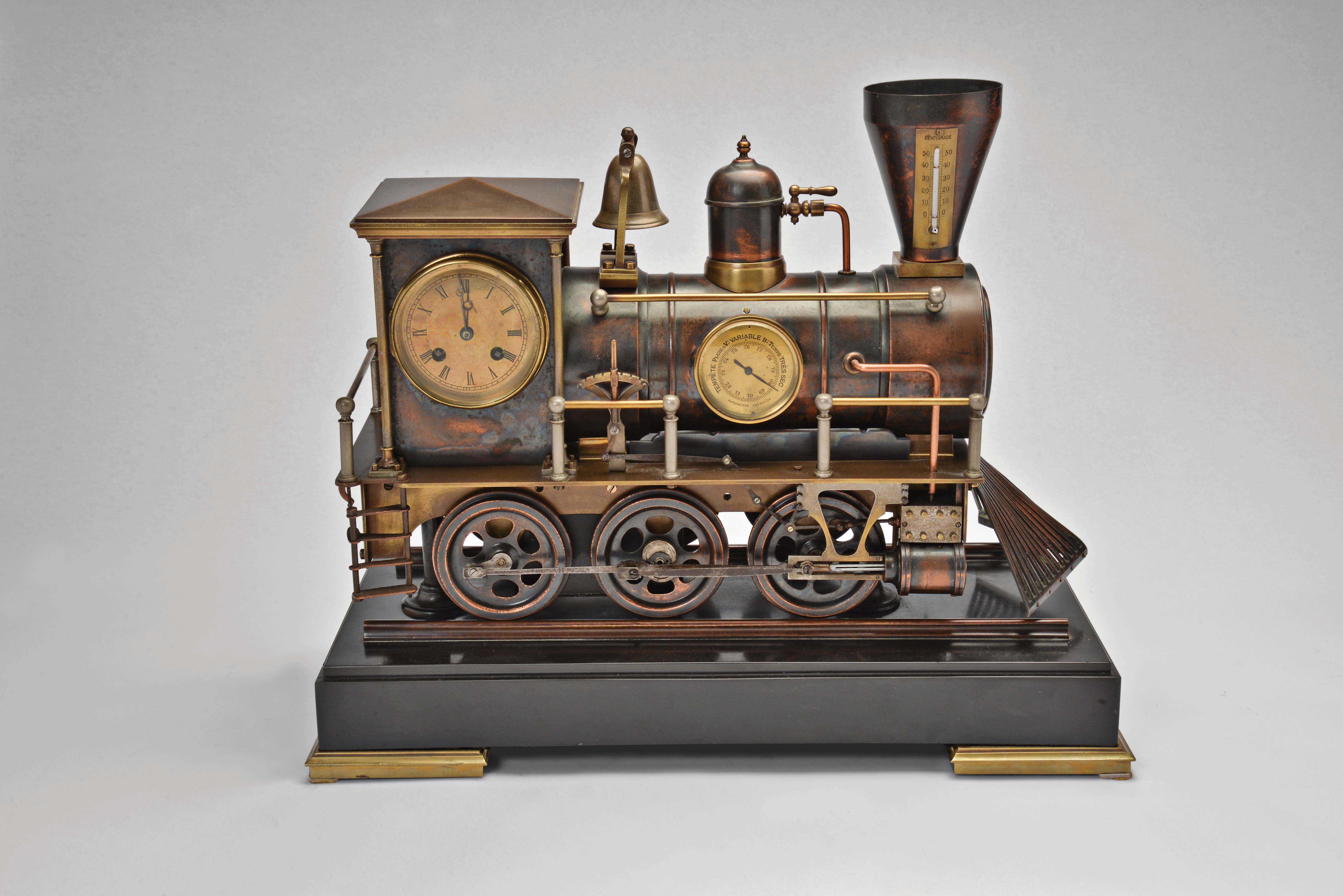 France, a rare, automated, patinated bronze locomotive form compendium, the stepped, black slate base on gilt feet with patinated rails below the large, steam locomotive, the darker surfaces highlighting the nickel, brass, and copper appointments, the engine front with cow catcher, the boiler with aneroid barometer, bell, steam dome with valve and flared stack with centigrade thermometer, the cab with shallow pitched roof, slender columns at the corners, and containing the clock and dial, a concealed movement in the base providing power to drive the six wheels, connecting rods, and piston, roman numeral brass dial, blued steel Breguet style hands, and 8 day, two train pendule de Paris movement — Antique Clocks Price Guide