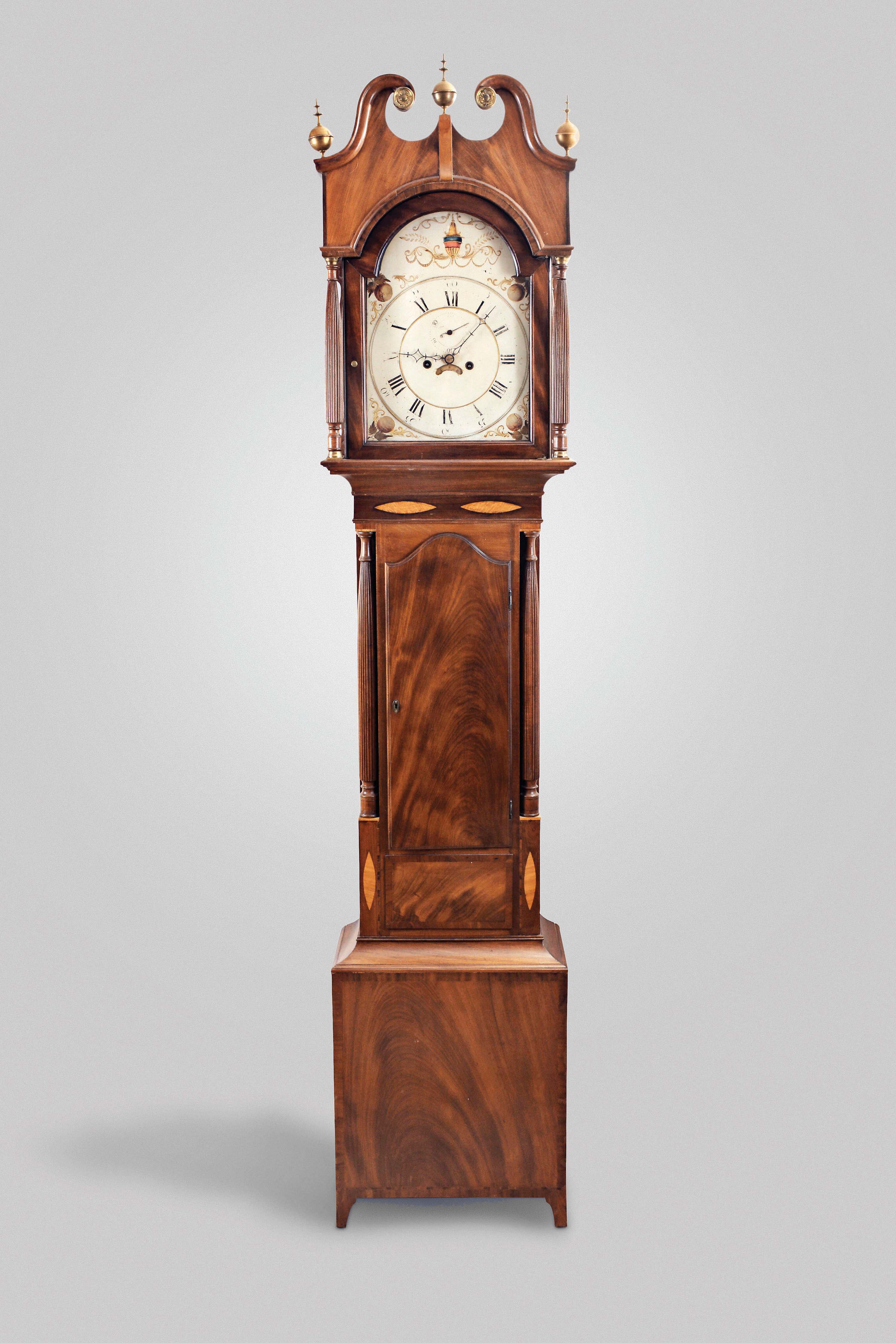 Unsigned New York or New Jersey, tall clock, 8 day, time and strike, weight driven movement in a inlaid mahogany case with high broken arch pediment top on hood with pressed brass rosettes and three brass finials. The painted metal dial is flanked by tapering full reeded columns with brass capitals up front and reeded quarter columns in the rear. The trunk has a crotch mahogany door flanked by similar full reeded columns over a crotch mahogany base framed by contrasting mahogany veneer resting on straight bracket feet. — Antique Clocks Price Guide