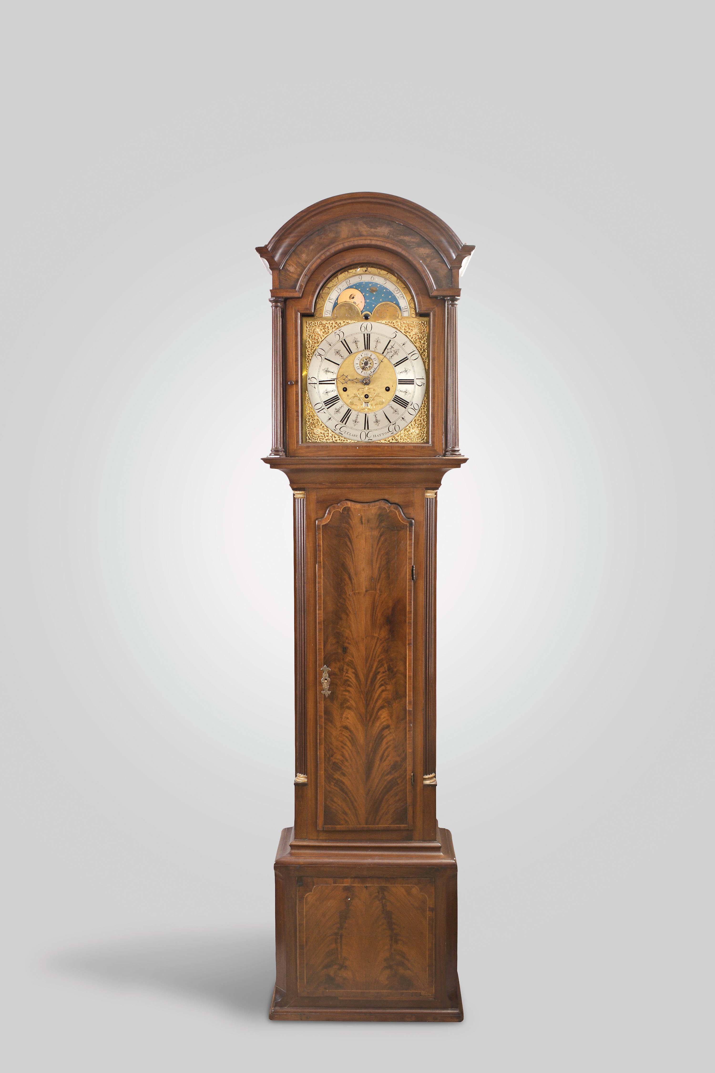 T. Clare, Hatton, England, tall clock, 8 day, time, strike and chime on a nest of six bells, weight driven movement in a inlaid mahogany case with four fluted columns flanking hood. The trunk has a shaped crotch mahogany door flanked by fluted quarter columns with gold painted capitals over a crotch mahogany base framed by string inlay and contrasting mahogany veneer. The brass dial has silvered chapter ring, moon phase, maker's signature, silvered second's bit and calendar aperture. — Antique Clocks Price Guide