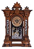William L. Gilbert Clock Co., Winsted, Conn., "Amphion" shelf clock with a spring driven, 8 day, time, strike and alarm movement in a walnut case with burl accents and cut glass mirror panels in the case adjacent to and below the door.