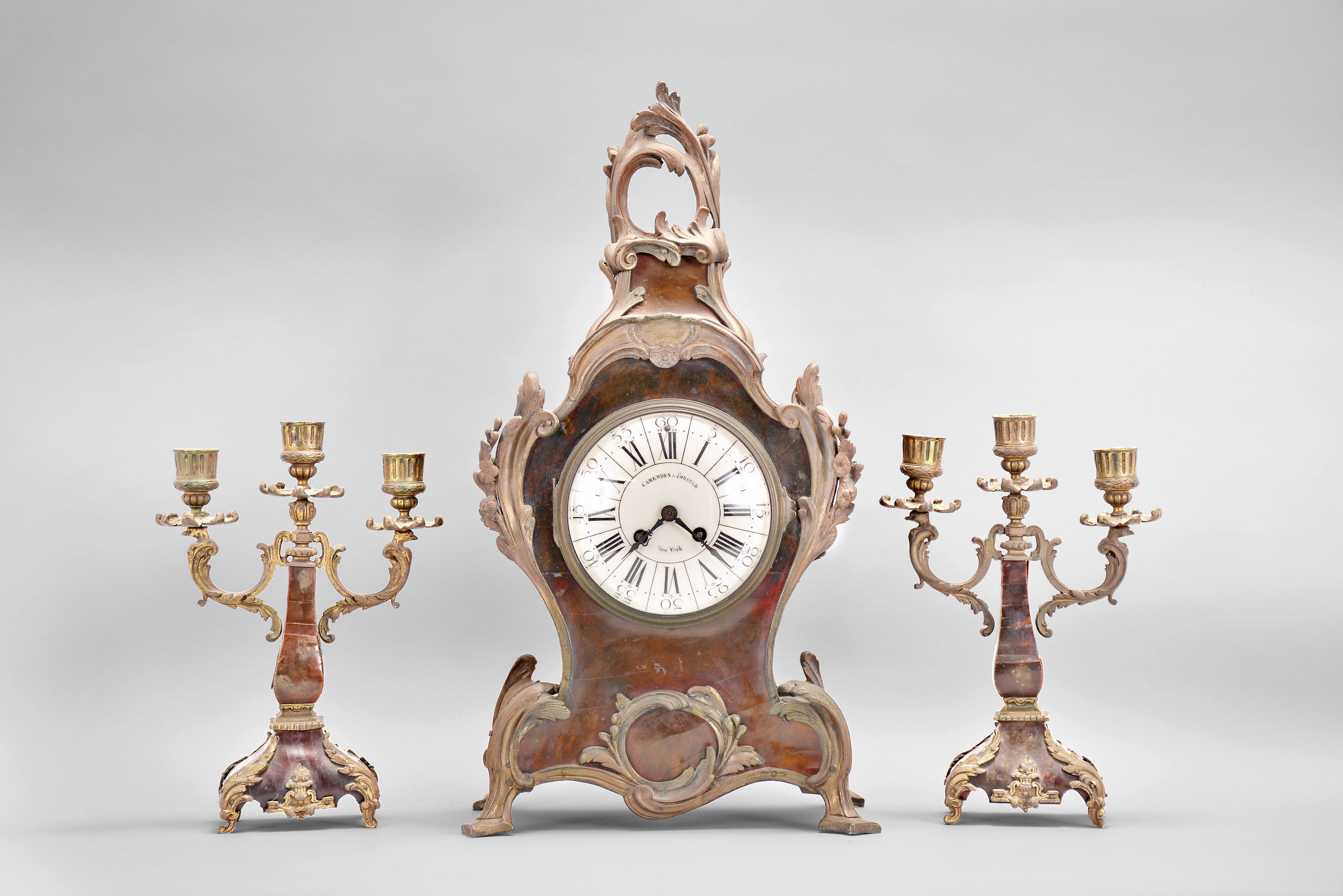 A.D. Mougin, Paris for Camerden & Forster of New York, mantel clock, 8 day, time and strike, spring driven pendule de Paris movement in a Louis XV style case with tortoise shell veneer and rococo style brass ornament, white enamel dial with retailer's name, steel hands, two matching candelabra holding 3 candles each. — Antique Clocks Price Guide
